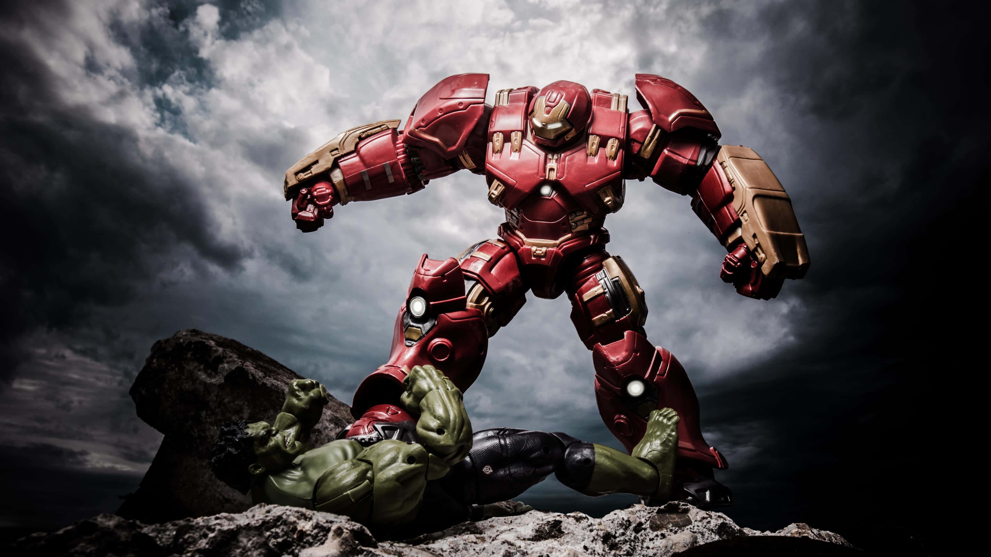 Iron Man Vs Hulk 桌布 壁紙 — 一套紅色和金色的Hulkbuster裝甲在風暴天空下的岩石懸崖上，勝利地站在被擊敗的綠色Hulk之上。