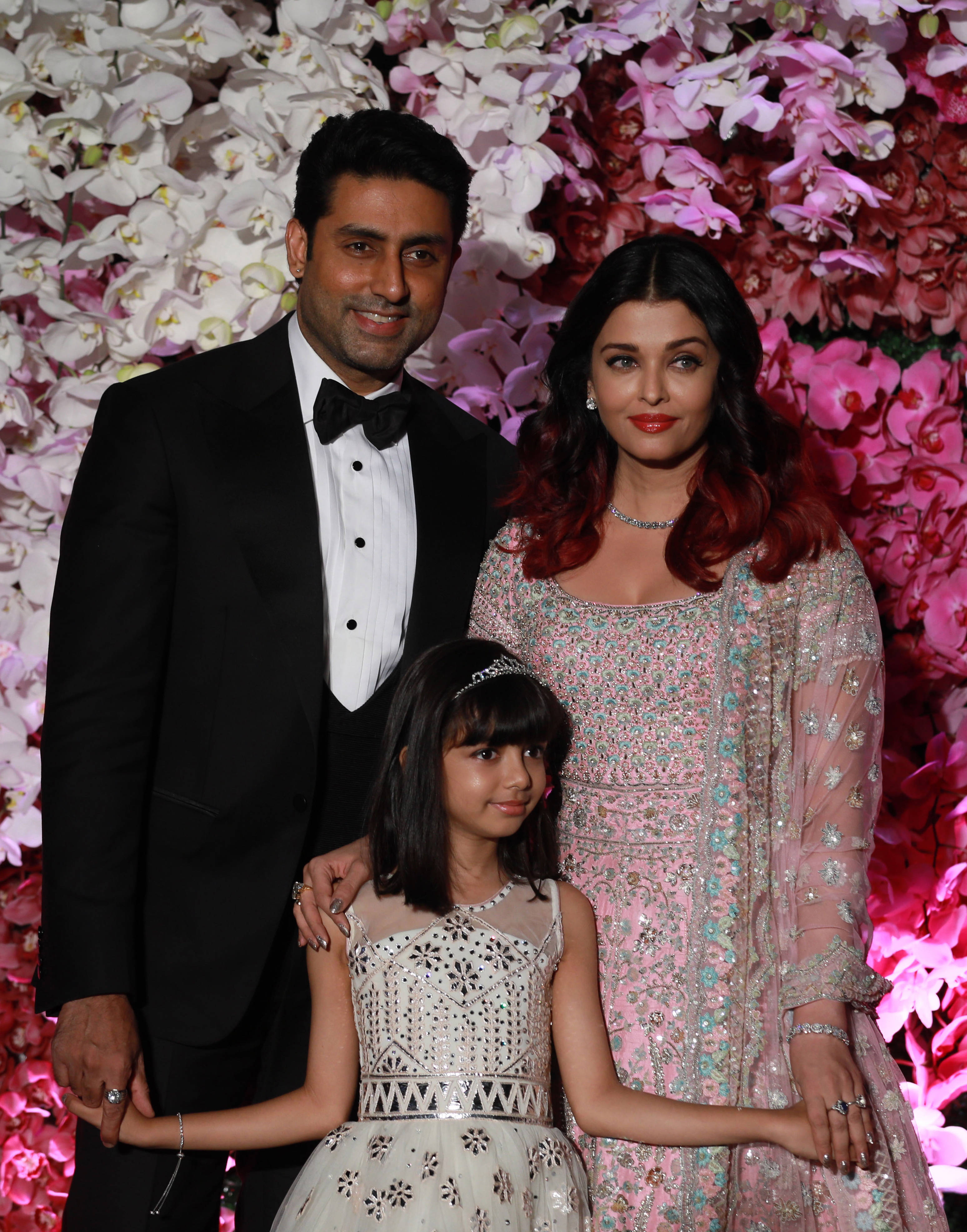 abhishek bachchan 桌布 壁紙 — 一家三口在正式活動中，在粉紅色和白色蘭花的鮮豔牆前優雅地擺姿勢。