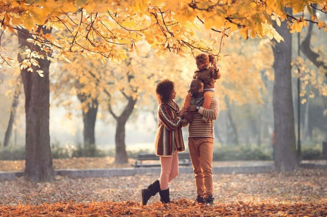 Fall Family 桌布 壁紙 — 一家三口在陽光明媚的公園裡，在金黃色的樹葉下分享歡樂的秋日時光。