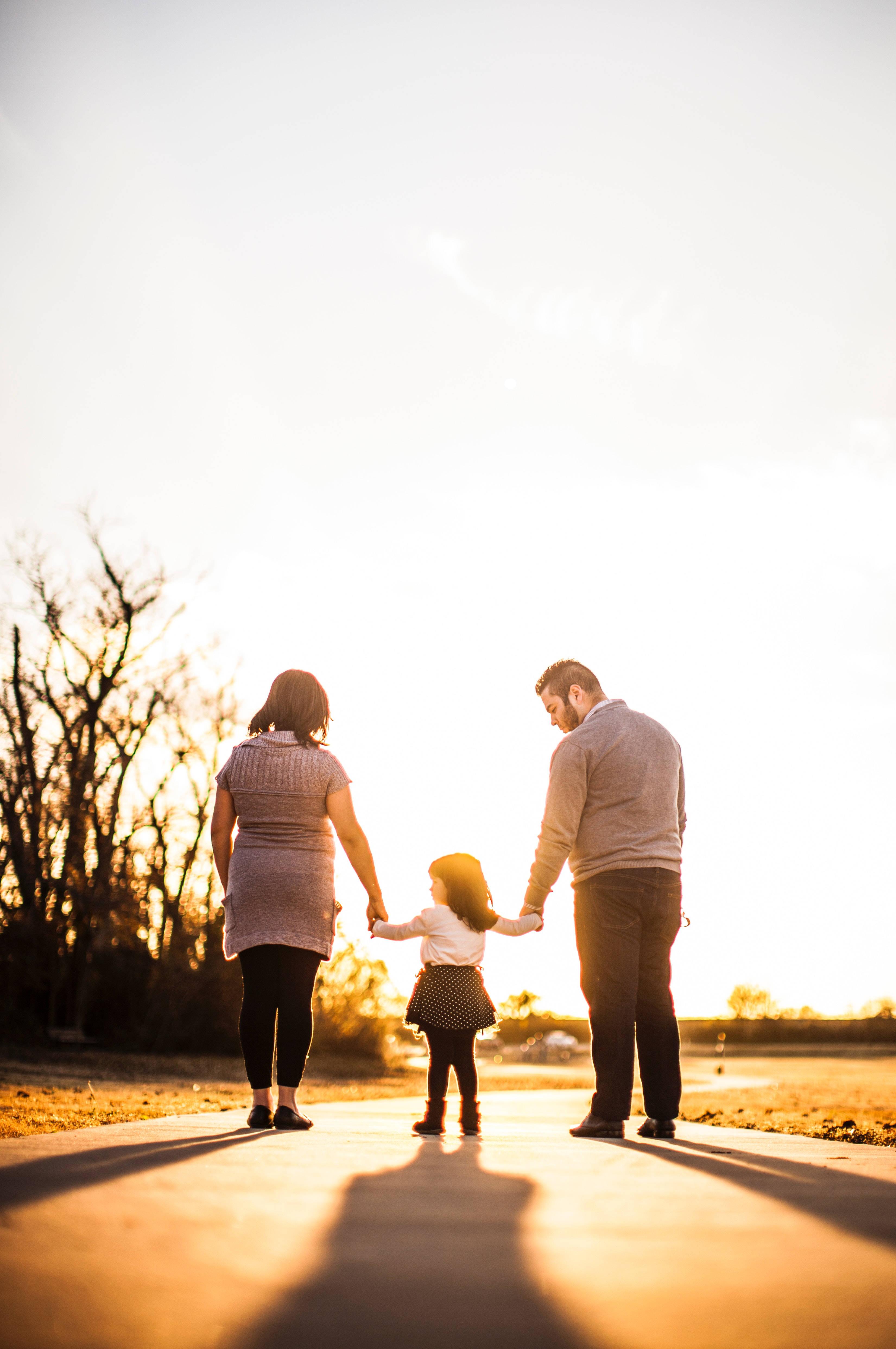 Family 桌布 壁紙 — 一家三口手牽手走在陽光明媚的小路上，正值黃金時刻，長長的影子在他們身後延伸。