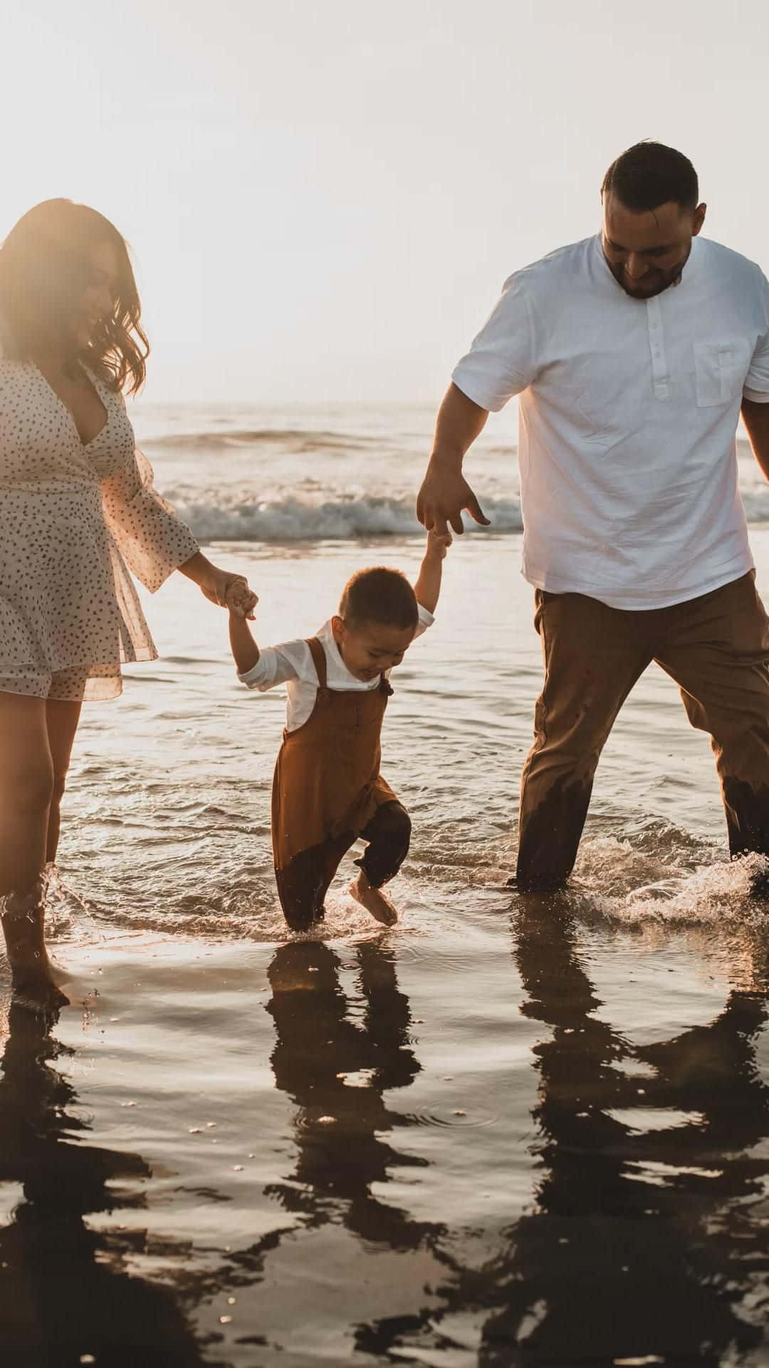 Family Beach 桌布 壁紙 — 一家三口手牽手走過淺海水域，正值黃金時刻，陽光照射的波浪和倒影。