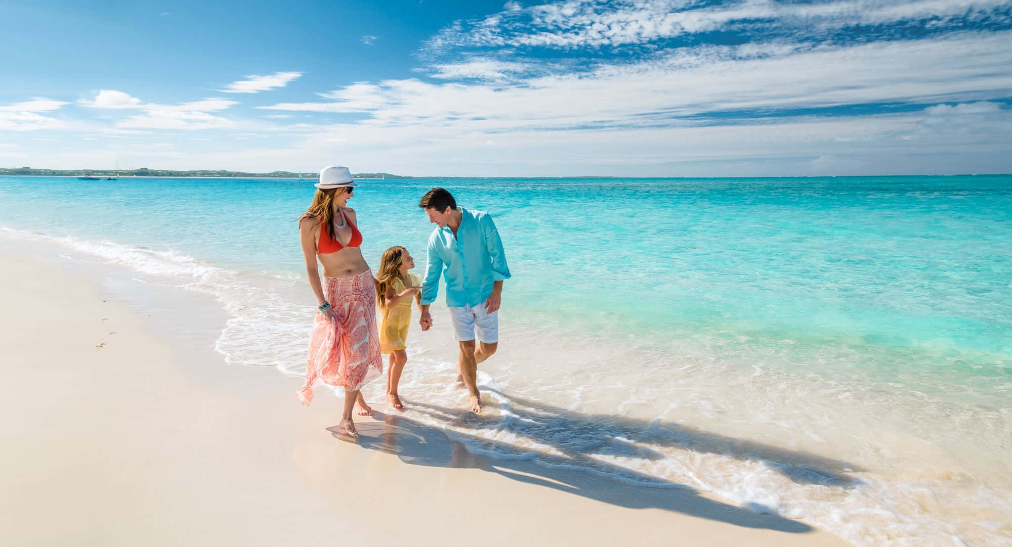 Beach Family 桌布 壁紙 — 一家三口赤腳走在純淨的白色沙灘上，碧綠的海浪拍打著他們的腳，頭頂是明亮的藍天。