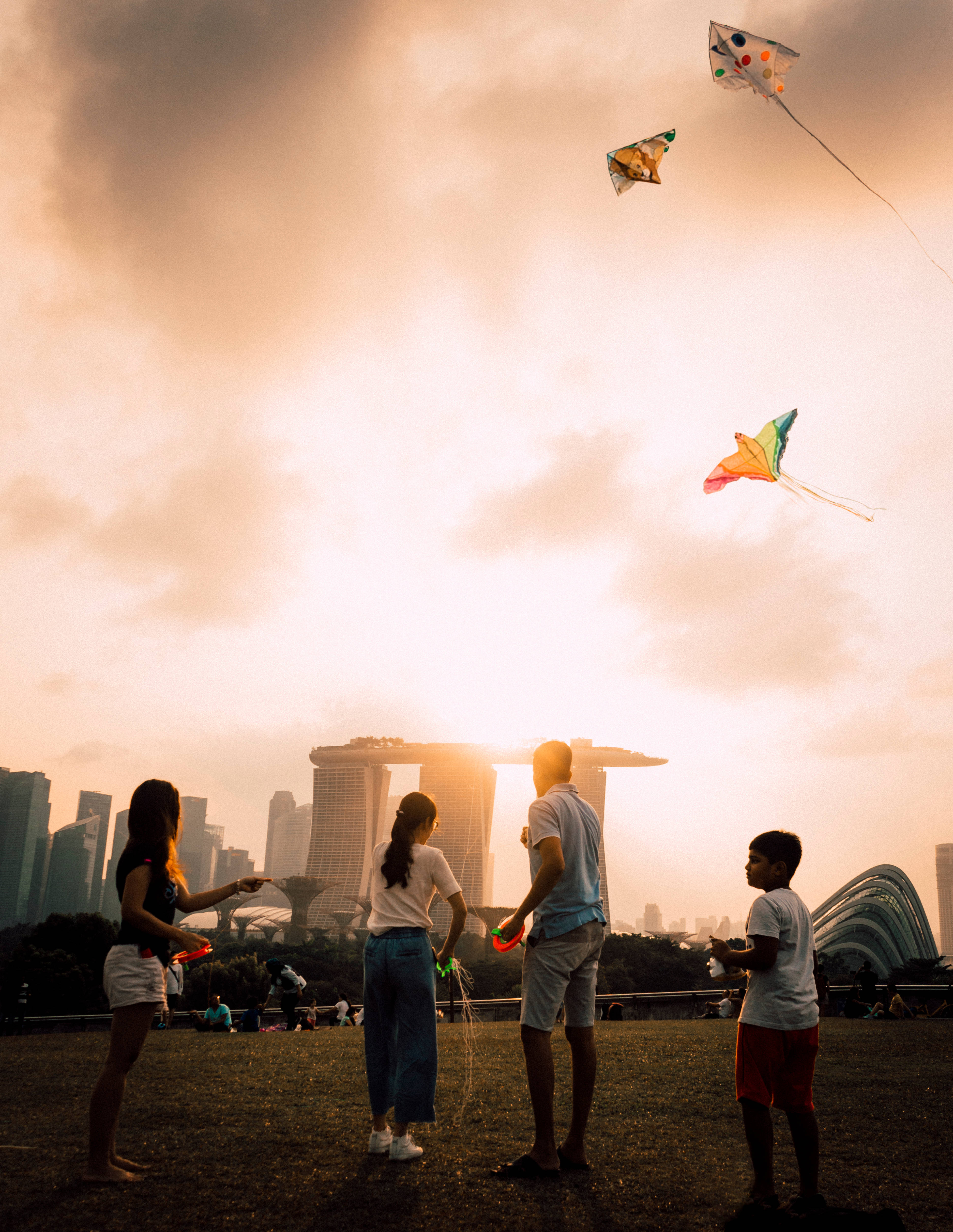 Singapore 桌布 壁紙 — 一家人在金色夕陽天空下放飛彩色風箏，背景是新加坡濱海灣金沙的天際線。