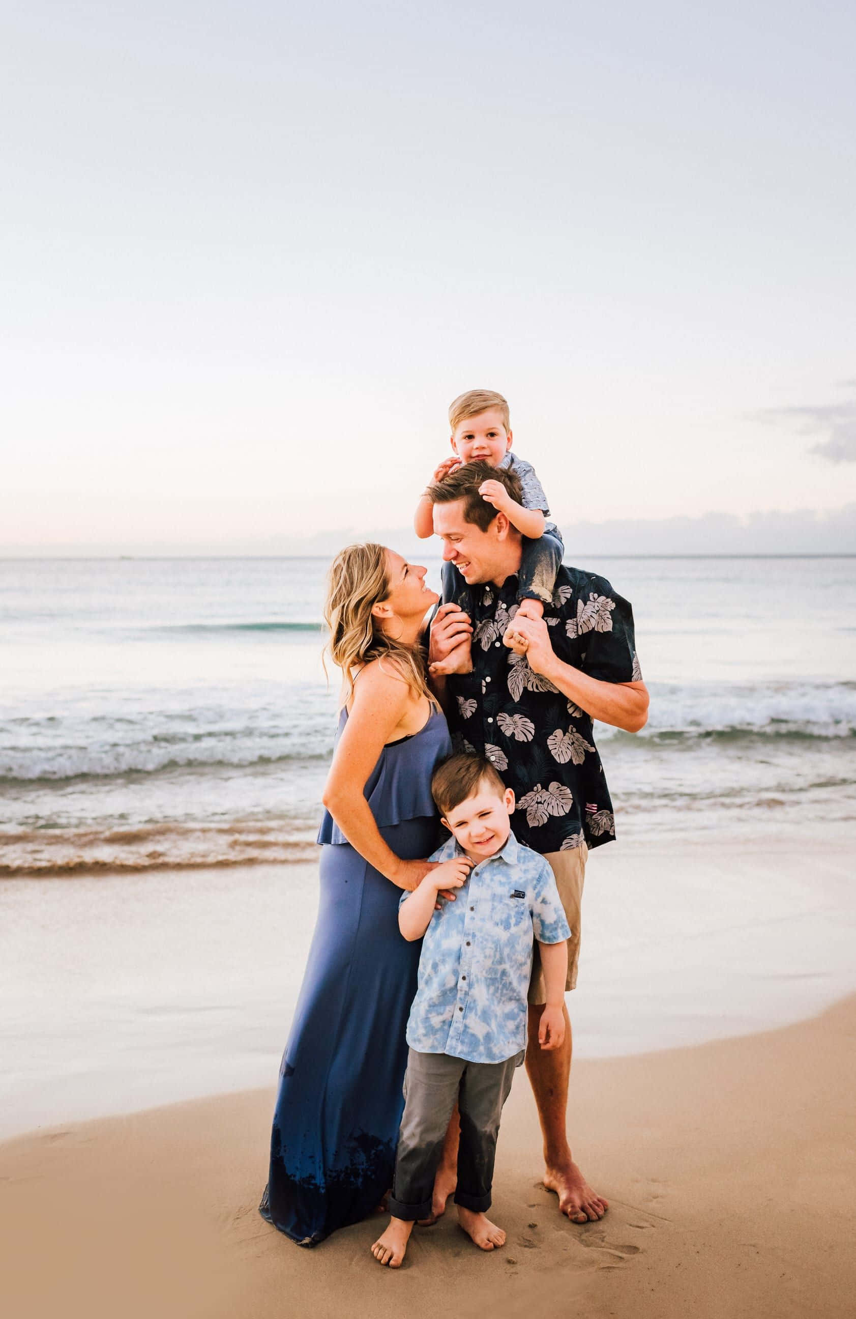 Family Beach 桌布 壁紙 — 一家四口在日落時分的沙灘上，背後有溫柔的海浪，開心地微笑。