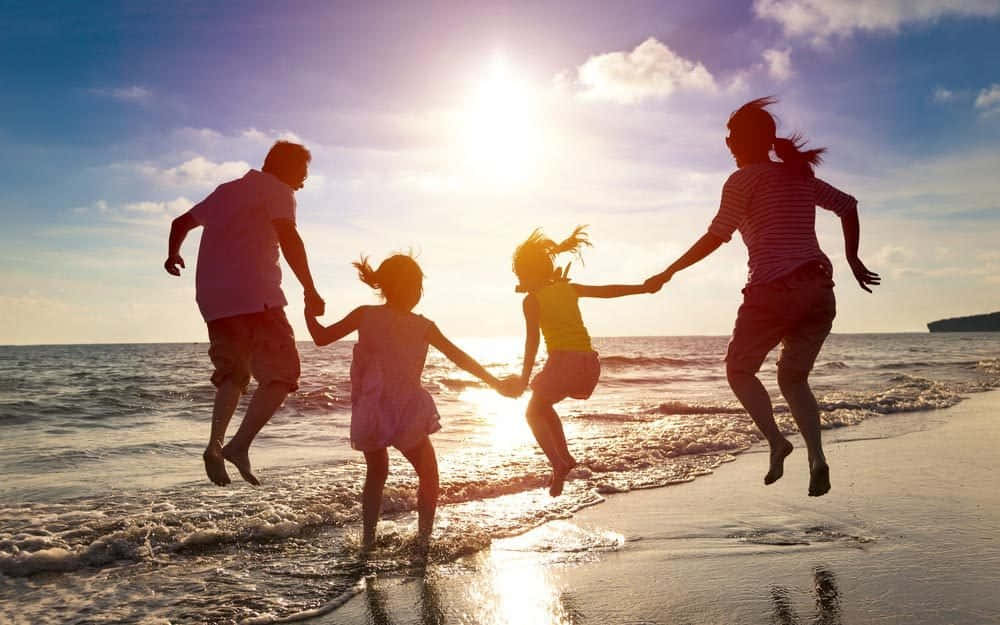 Beach Family 桌布 壁紙 — 一家四口在陽光明媚的海灘上歡樂地齊齊跳躍，金色海浪在他們腳下拍打。
