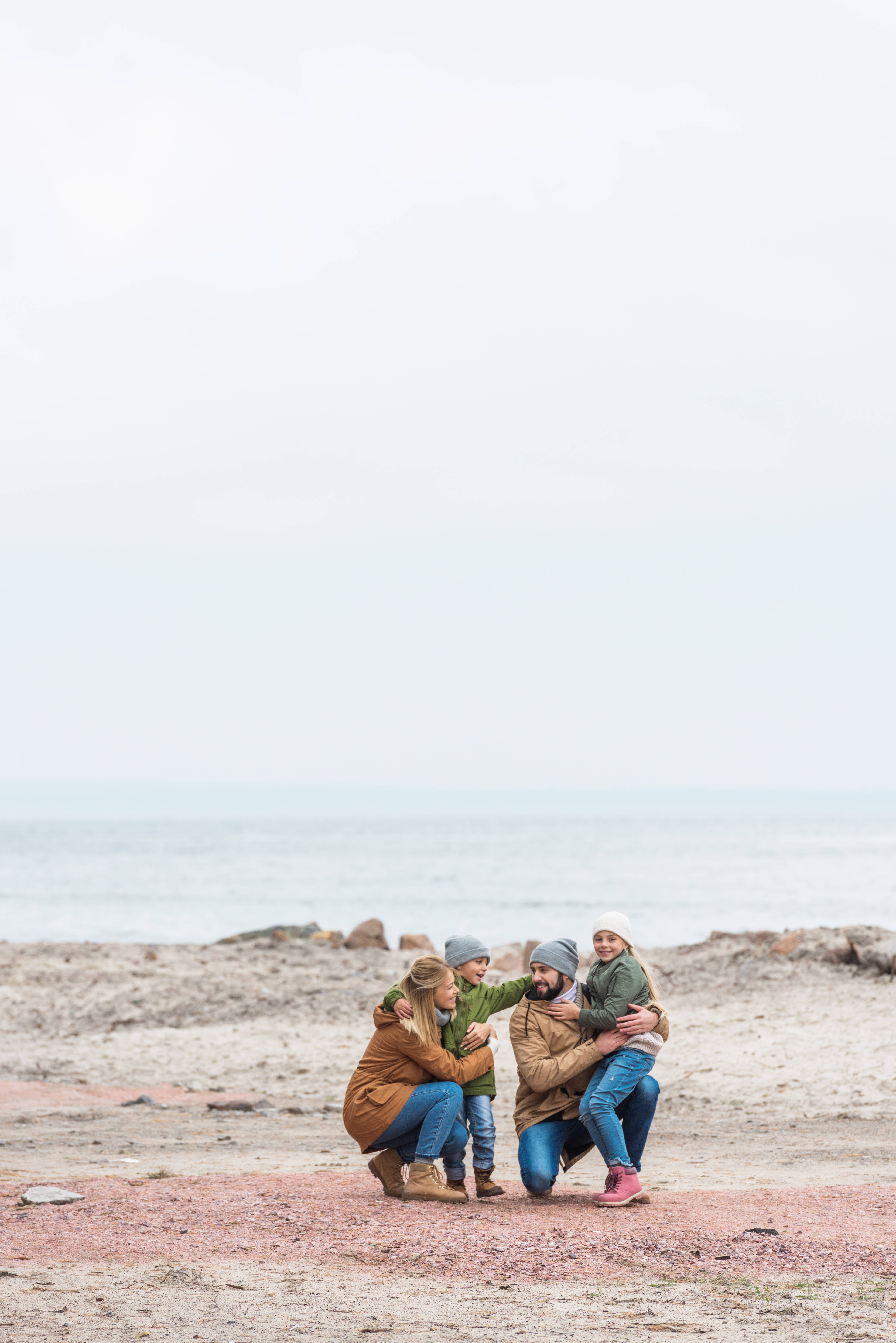 Family 桌布 壁紙 — 一家四口在霧濛濛的海灘上溫暖地擁抱，平靜的海水延伸至地平線。