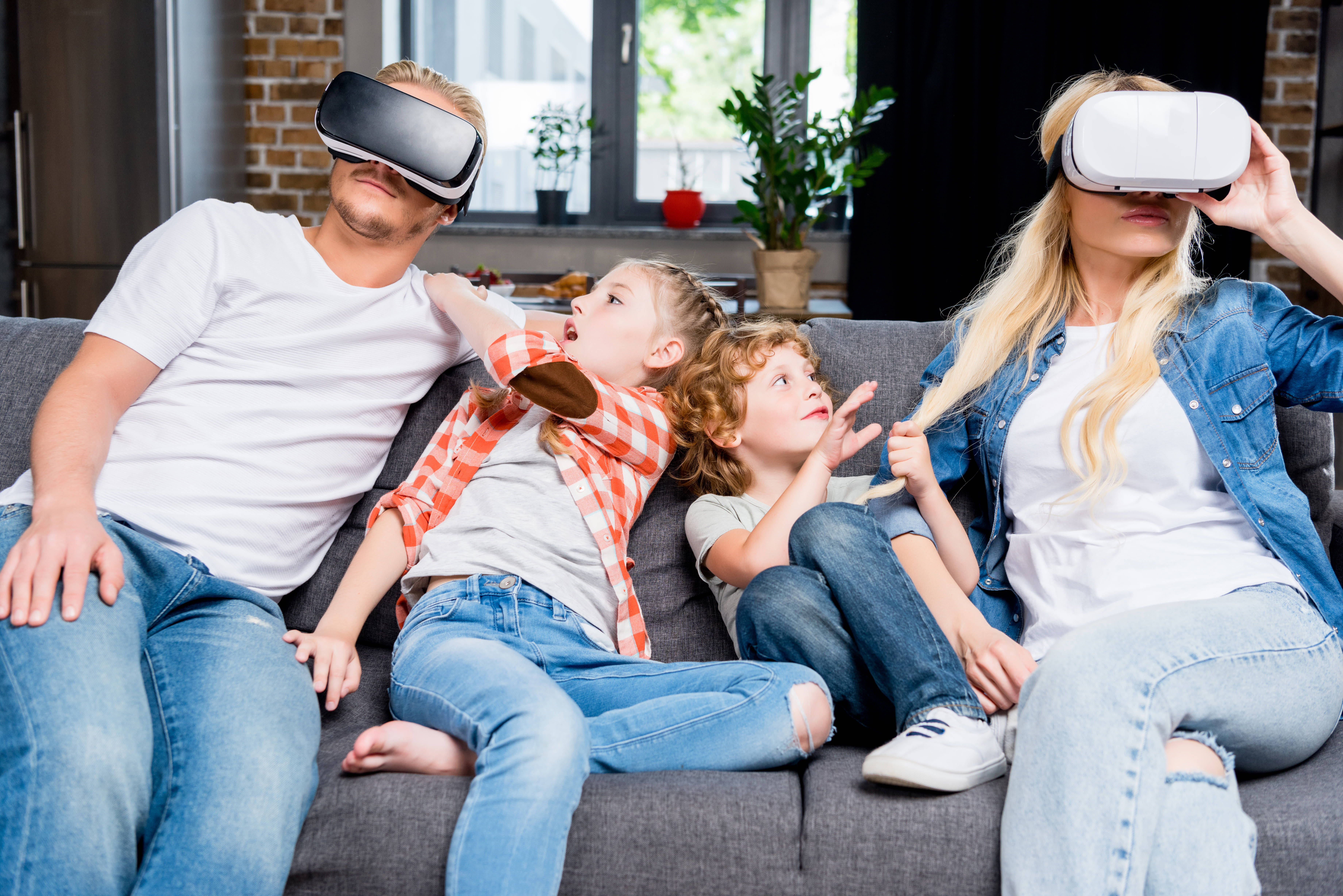 Family 桌布 壁紙 — 一家四口坐在沙發上戴著VR頭盔，兩個孩子興奮地指向虛擬體驗並做手勢。