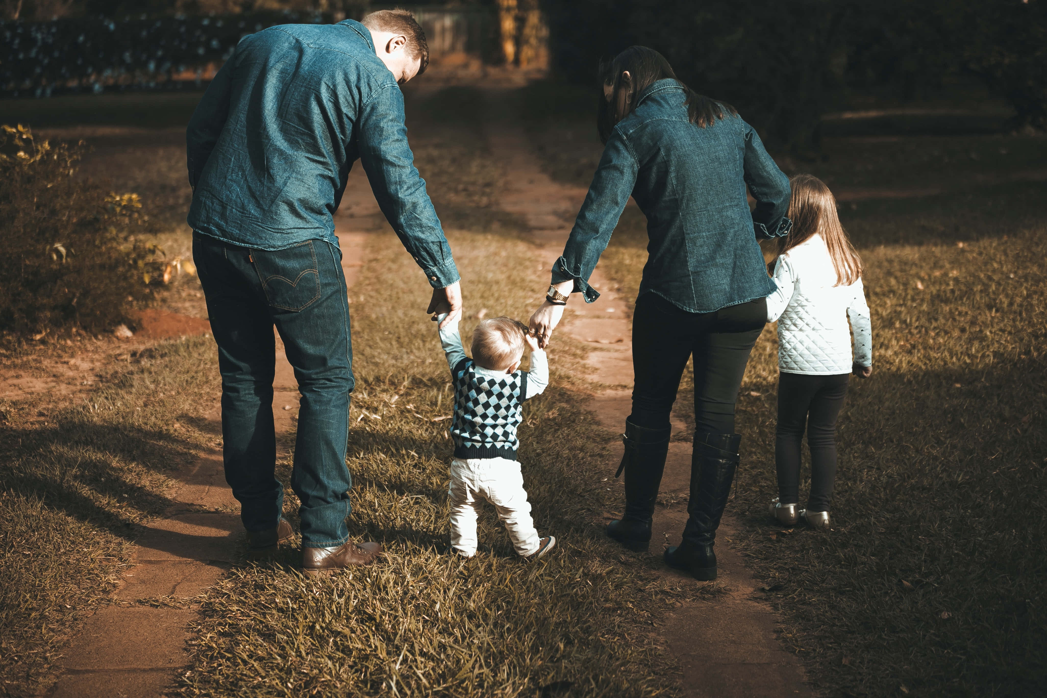 Mom 桌布 壁紙 — 一家四口手牽手，在黃金時段陽光普照的草地公園中，沿著一條泥土路行走。