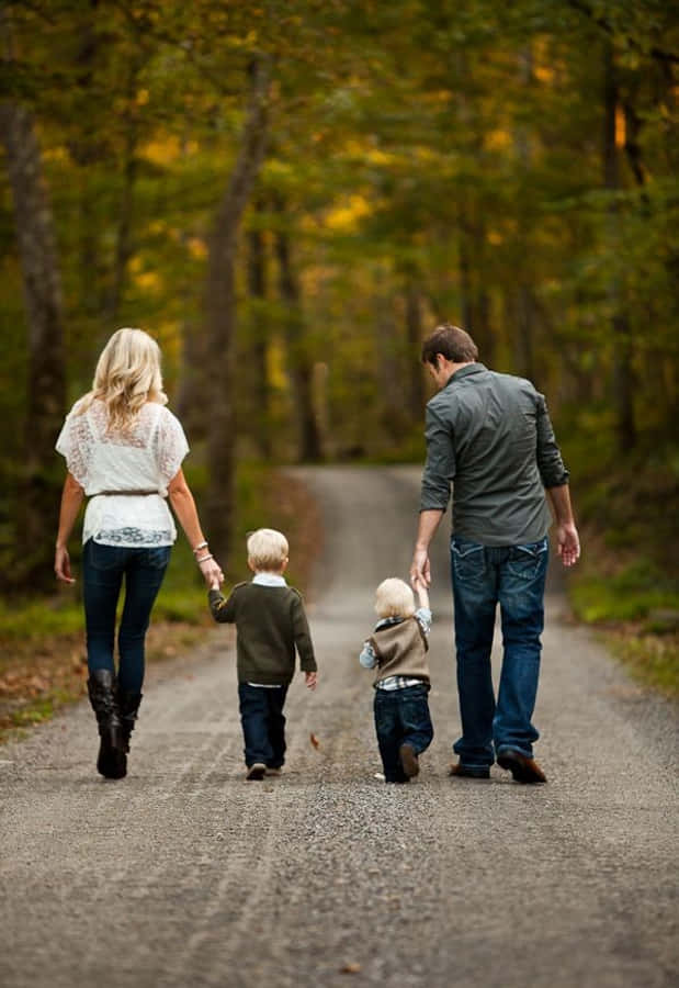 Family 桌布 壁紙 — 一家四口手牽手，沿著一條碎石路穿過充滿活力的秋日森林。