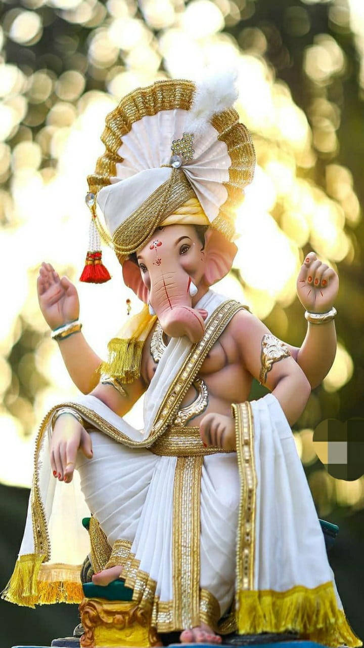 ganesh iPhone 桌布 壁紙 — 一尊以白色和金色鮮豔裝飾的象頭神雕像，在發光的散景背景前靜靜地坐著。