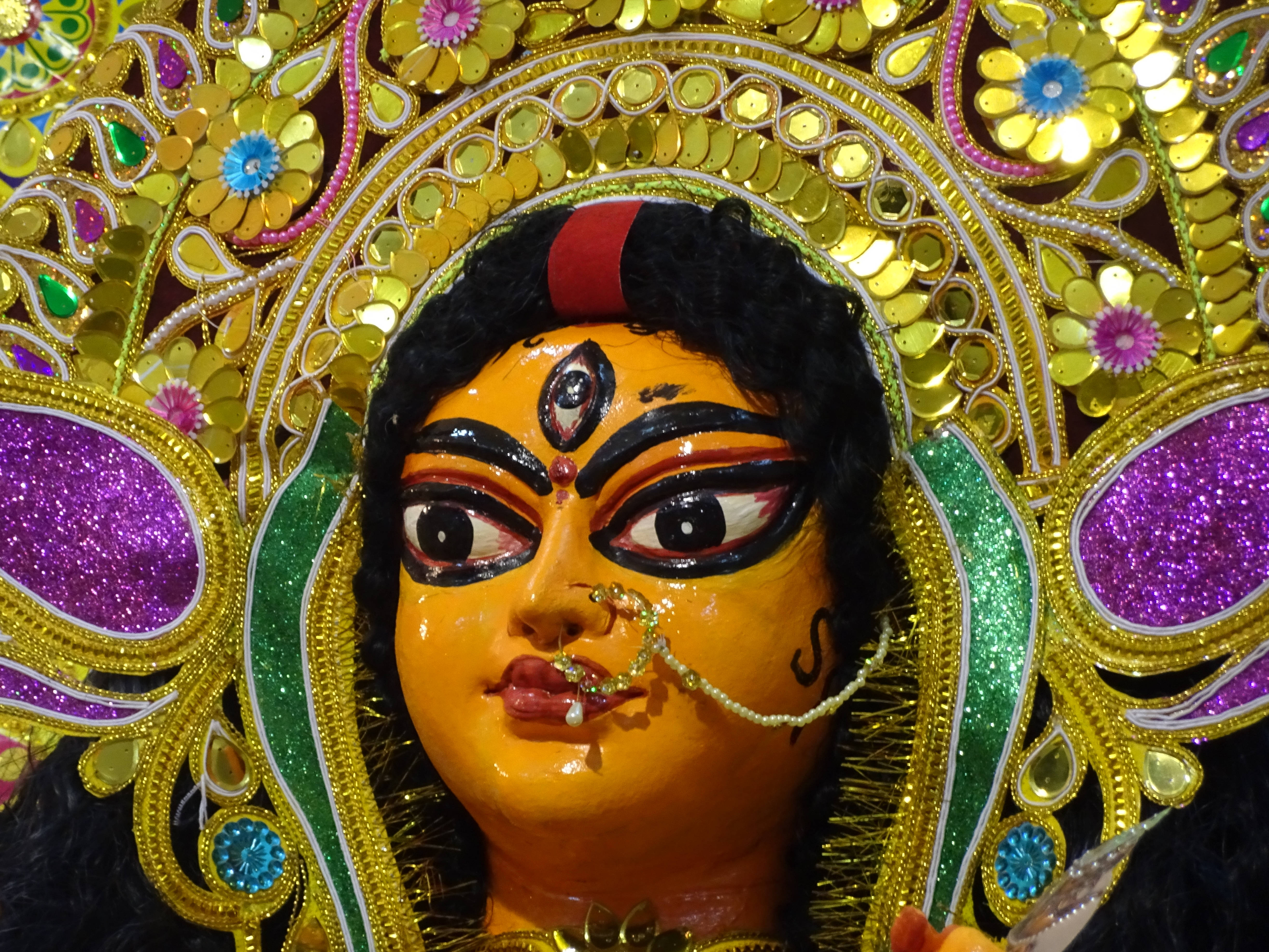 maa durga 桌布 壁紙 — 一尊充滿活力的金色杜爾迦雕像，帶有精緻的花卉頭飾和閃閃發光的紫色點綴。