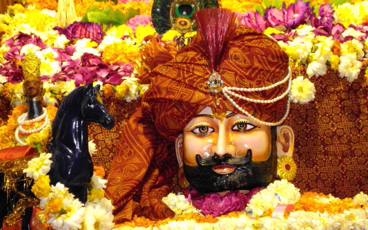 Shyam Baba 桌布 壁紙 — 一尊充滿活力的鬍鬚神像，裝飾著濃郁的橙色頭巾，周圍環繞著色彩繽紛的花環。