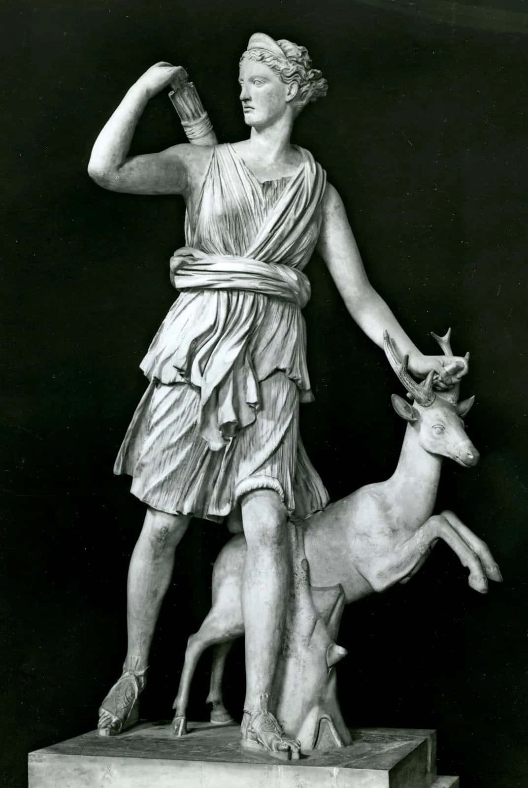 greek 桌布 壁紙 — 一尊古典大理石雕像，描繪一位披著長袍的女性形象站在一隻後腿站立的鹿旁邊，背景為深色。
