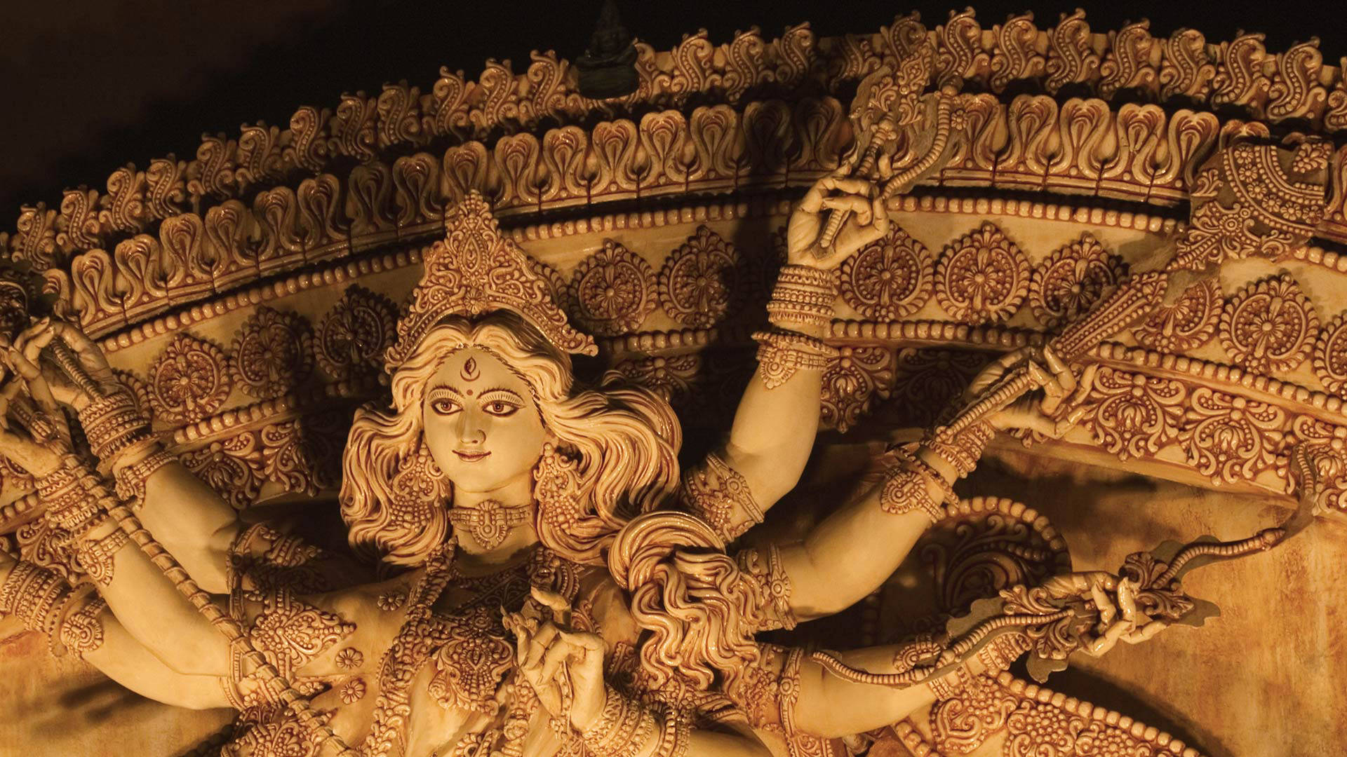 Kolkata 桌布 壁紙 — 一尊多臂印度女神的金色雕像，飾有精緻珠寶和華麗圖案，在溫暖燈光下閃耀。