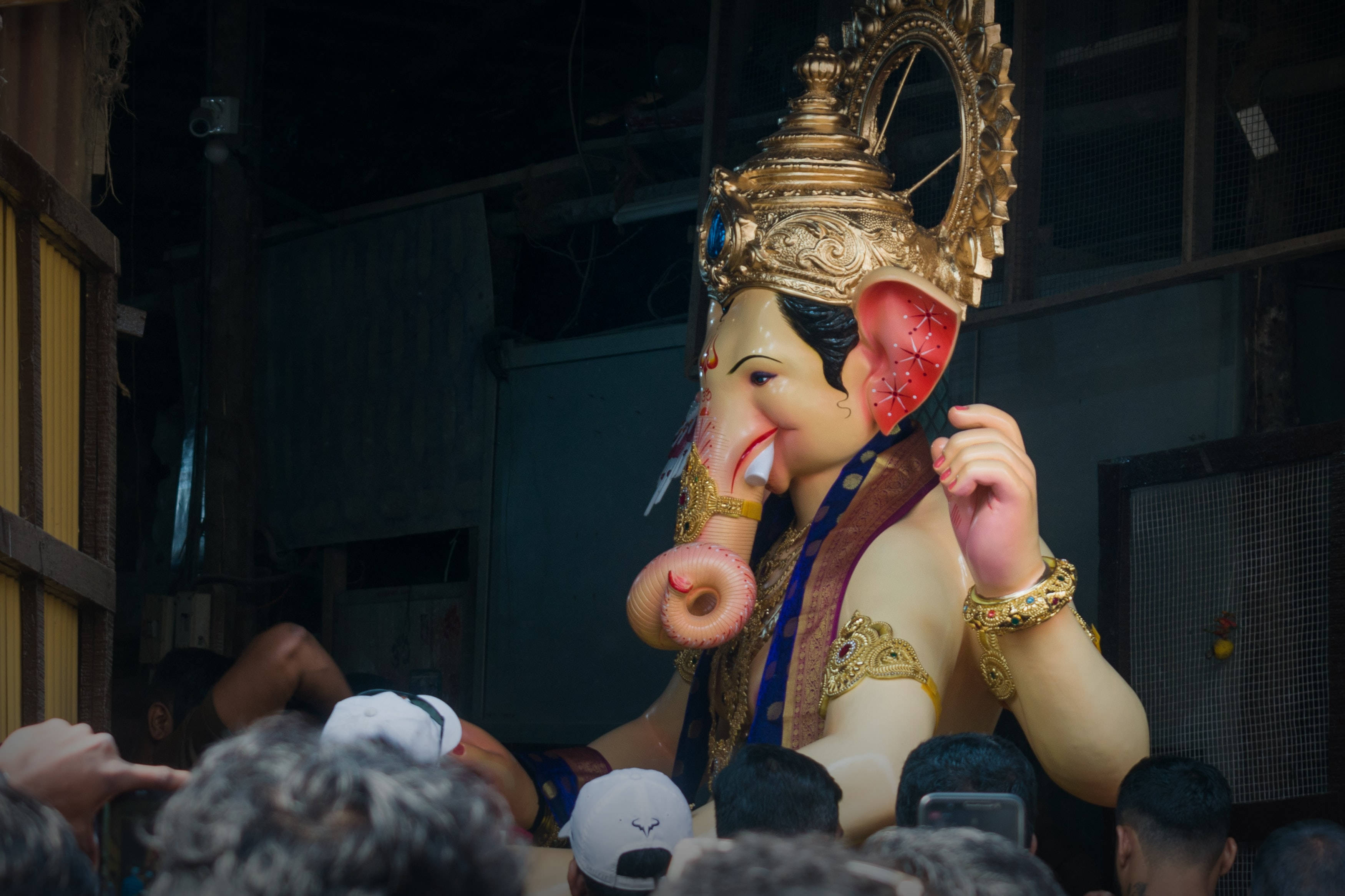 Hindu Temple 桌布 壁紙 — 一尊大型發光的象頭神像，戴著金色皇冠和紅色耳朵，夜晚被人群包圍。