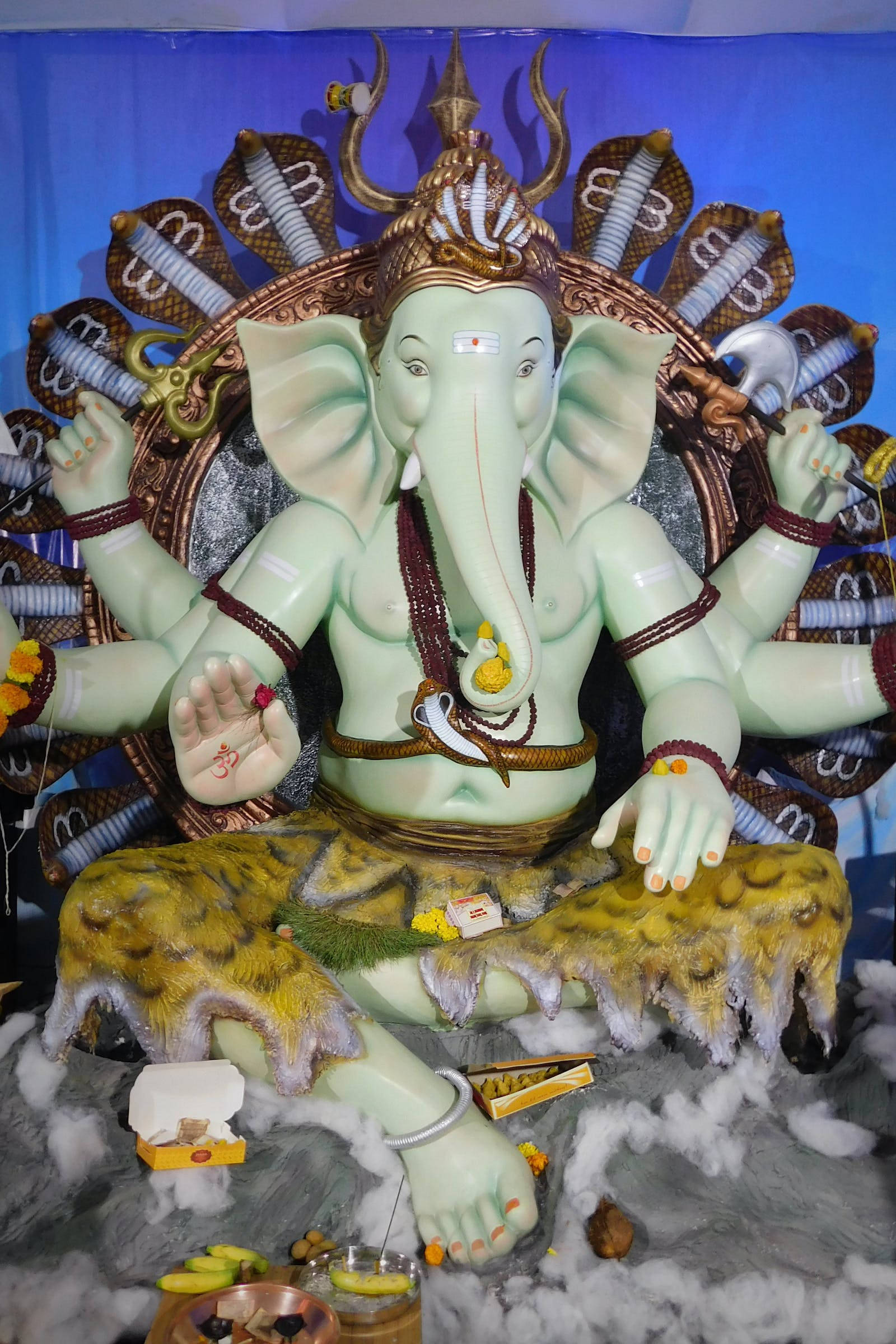 Vinayaka 桌布 壁紙 — 一尊大型綠色象頭神像，有多隻手臂和皇冠，坐在飾有眼鏡蛇和供品的寶座上。