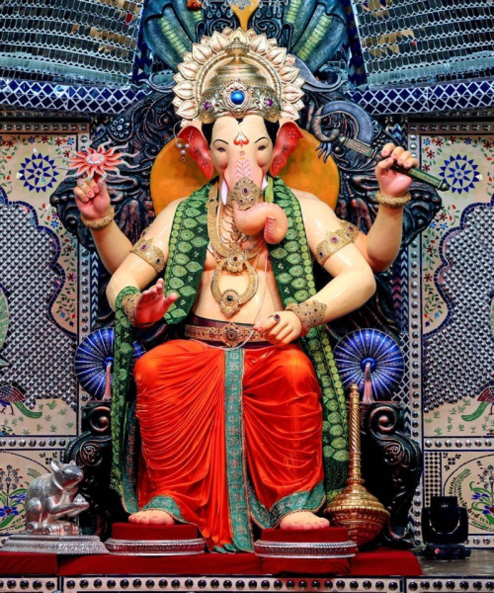 Hindu Temple 桌布 壁紙 — 一尊宏偉的坐姿象頭神像，裝飾著鮮豔的紅綠色長袍和精緻的金飾，背景是色彩繽紛的馬賽克。