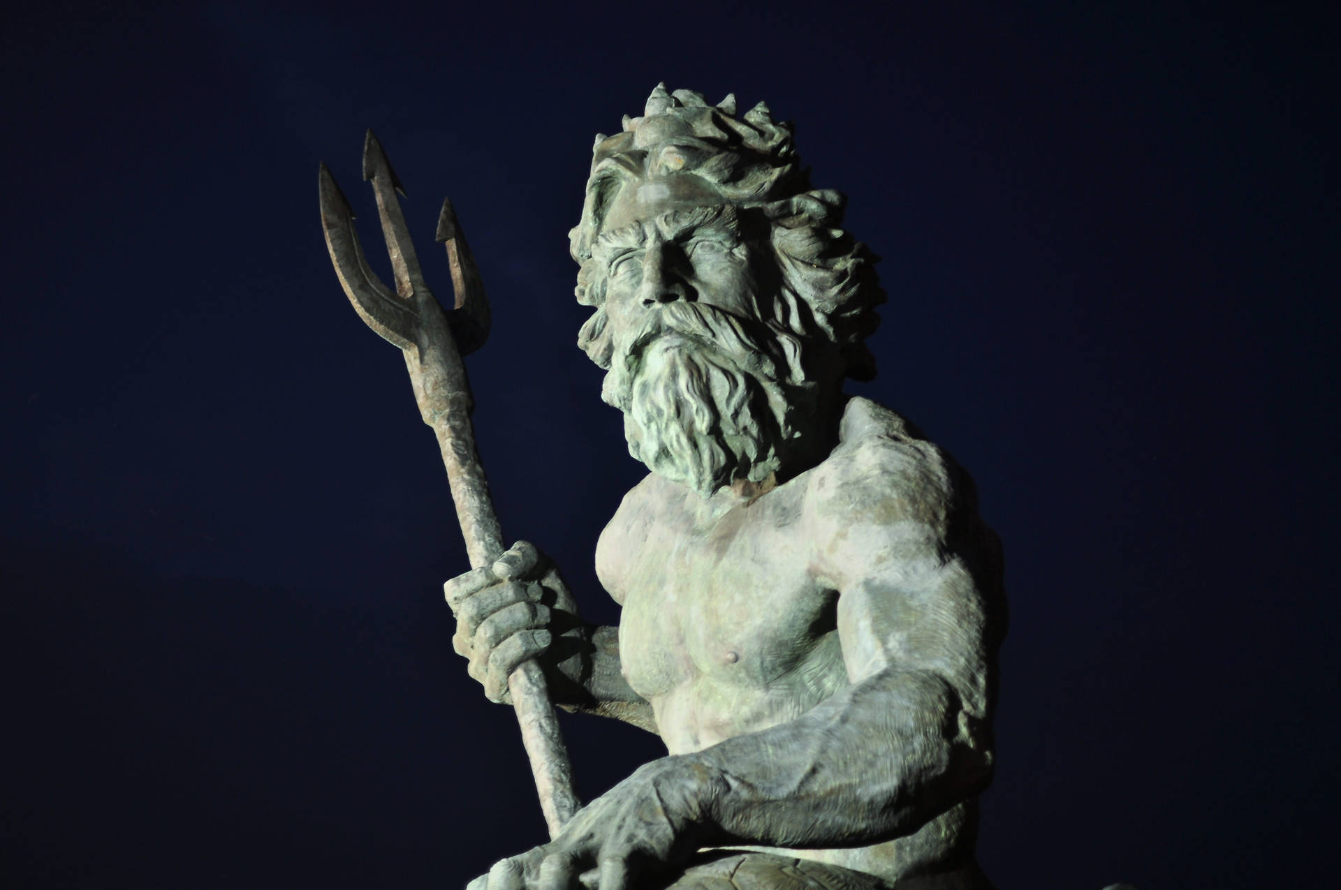 Statue Aesthetic 桌布 壁紙 — 一尊宏偉的尼普頓青銅像手持三叉戟，在深邃的夜空下被照亮。