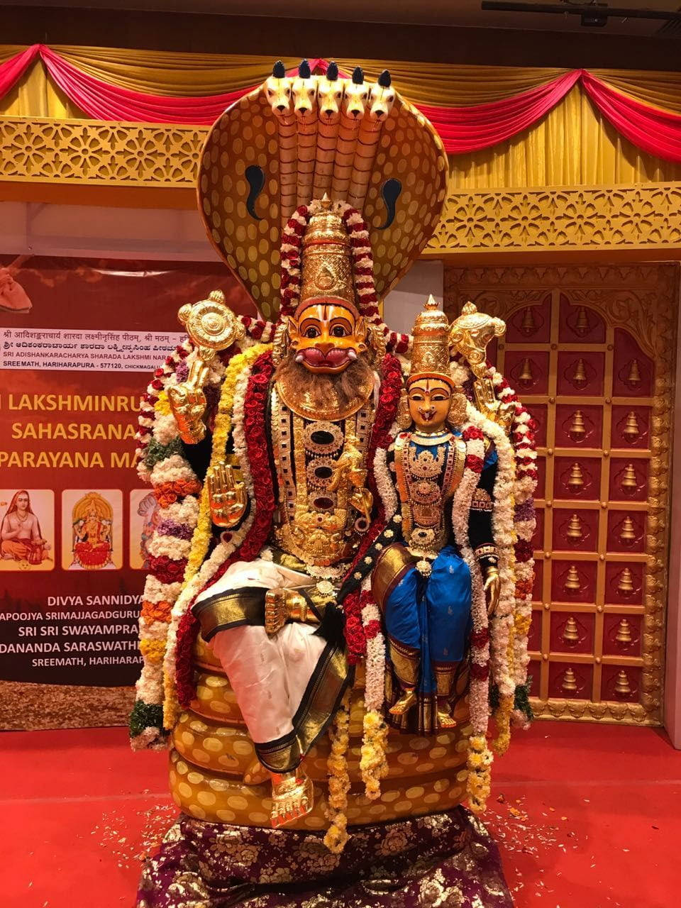 vishnu HD 桌布 壁紙 — 一尊宏偉的金色濕婆神像，帶有眼鏡蛇頭罩，伴侶帕爾瓦蒂裝飾著鮮花和珠寶，立於紅地毯上。