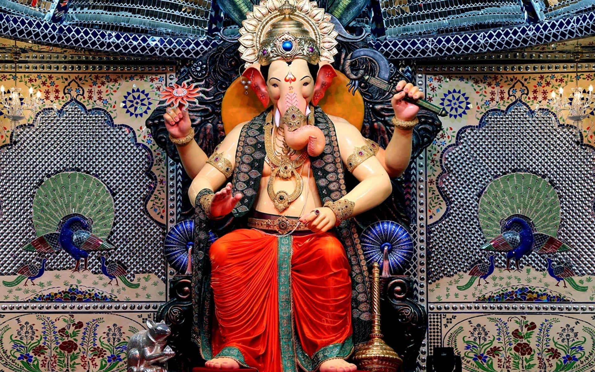 Ganesh 桌布 壁紙 — 一尊宏偉的金色象神像坐在華麗的藍色和金色裝飾中，帶有孔雀圖案和花卉圖案。