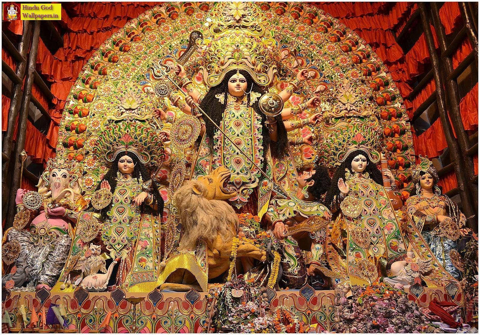 神 桌布 壁紙 — 一尊宏偉華麗的杜爾迦雕像，有多隻手臂和武器，被女神和神話生物環繞，下方是鮮紅色的華蓋。