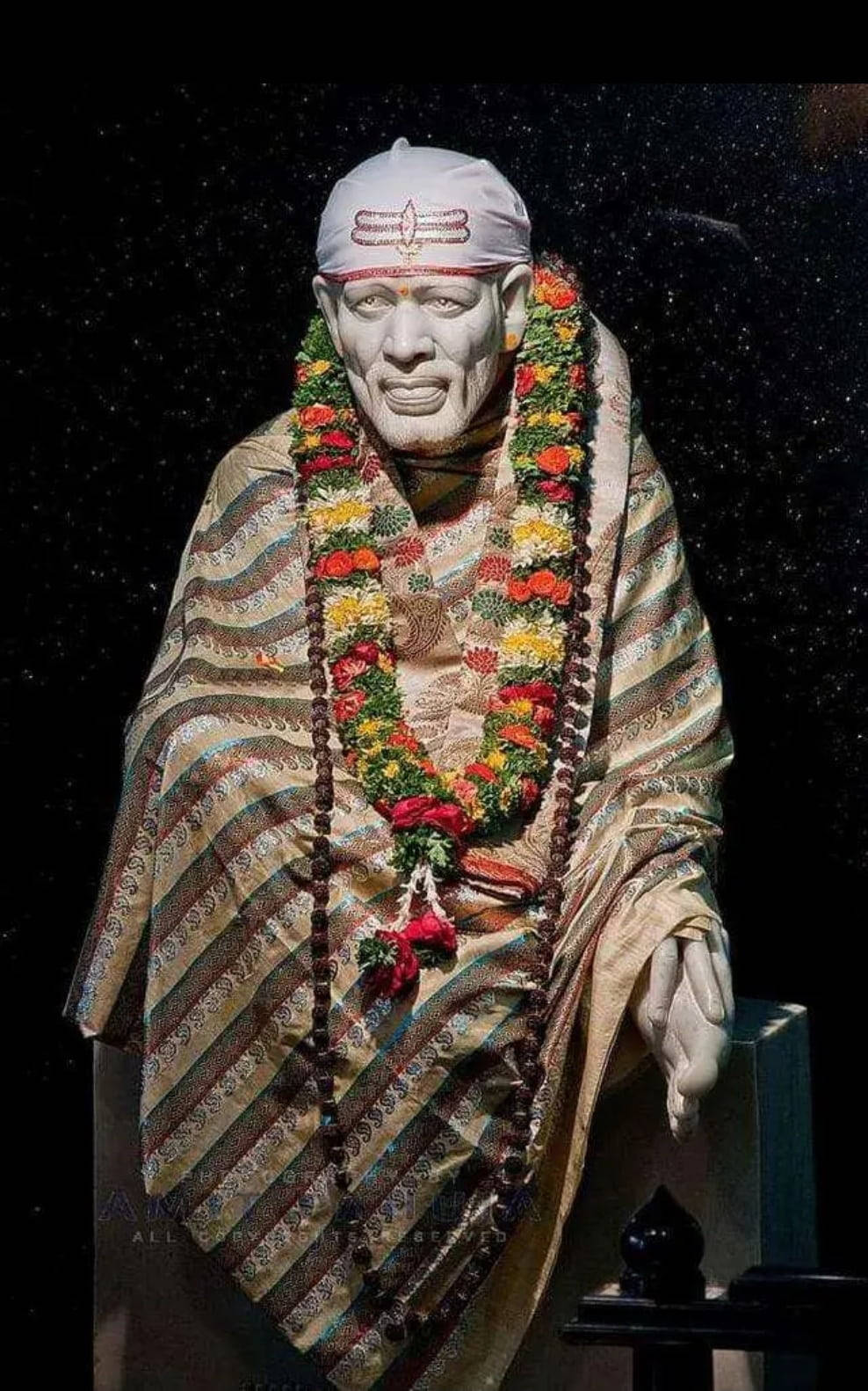 在繁星點點的夜空下，一位精神人物雕像戴著花環和條紋長袍。 — Sai Baba 高畫質壁紙 壁紙