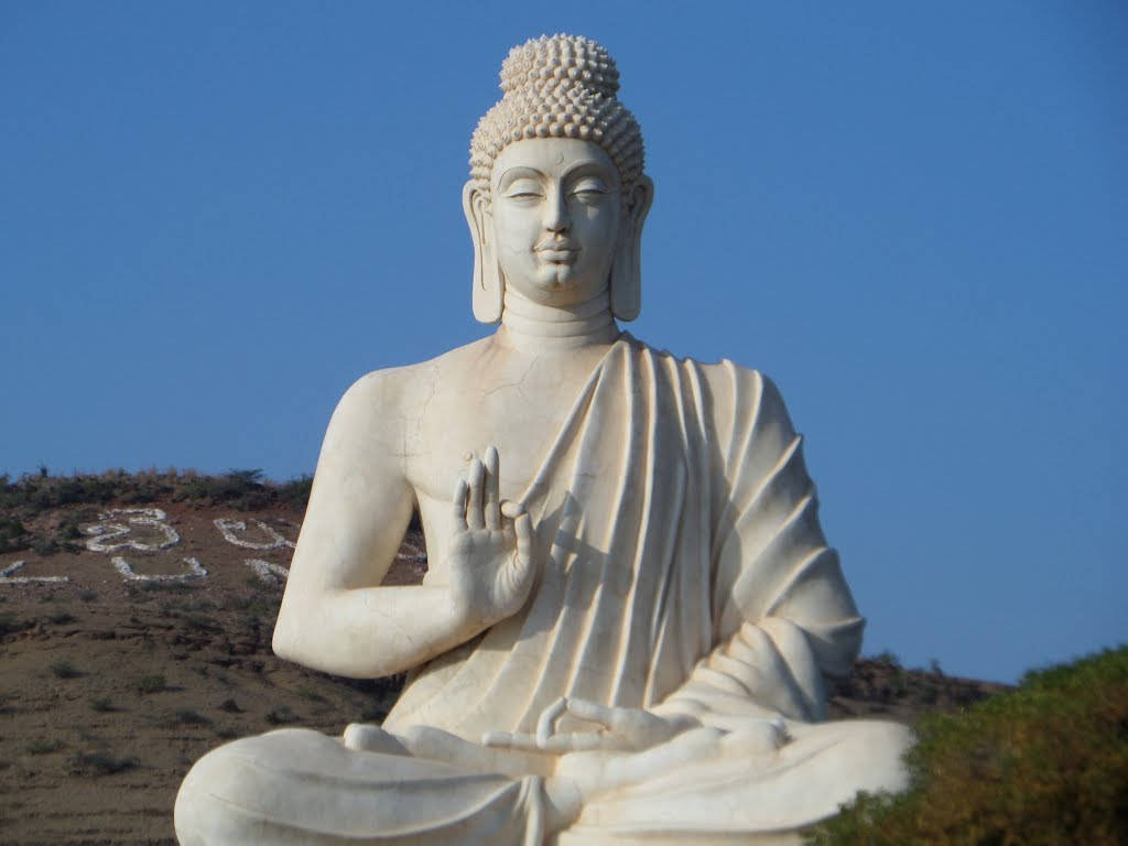 god laptop 桌布 壁紙 — 一尊寧靜的白色佛像在清澈的藍天下冥想，背後的山坡上有白色符號。