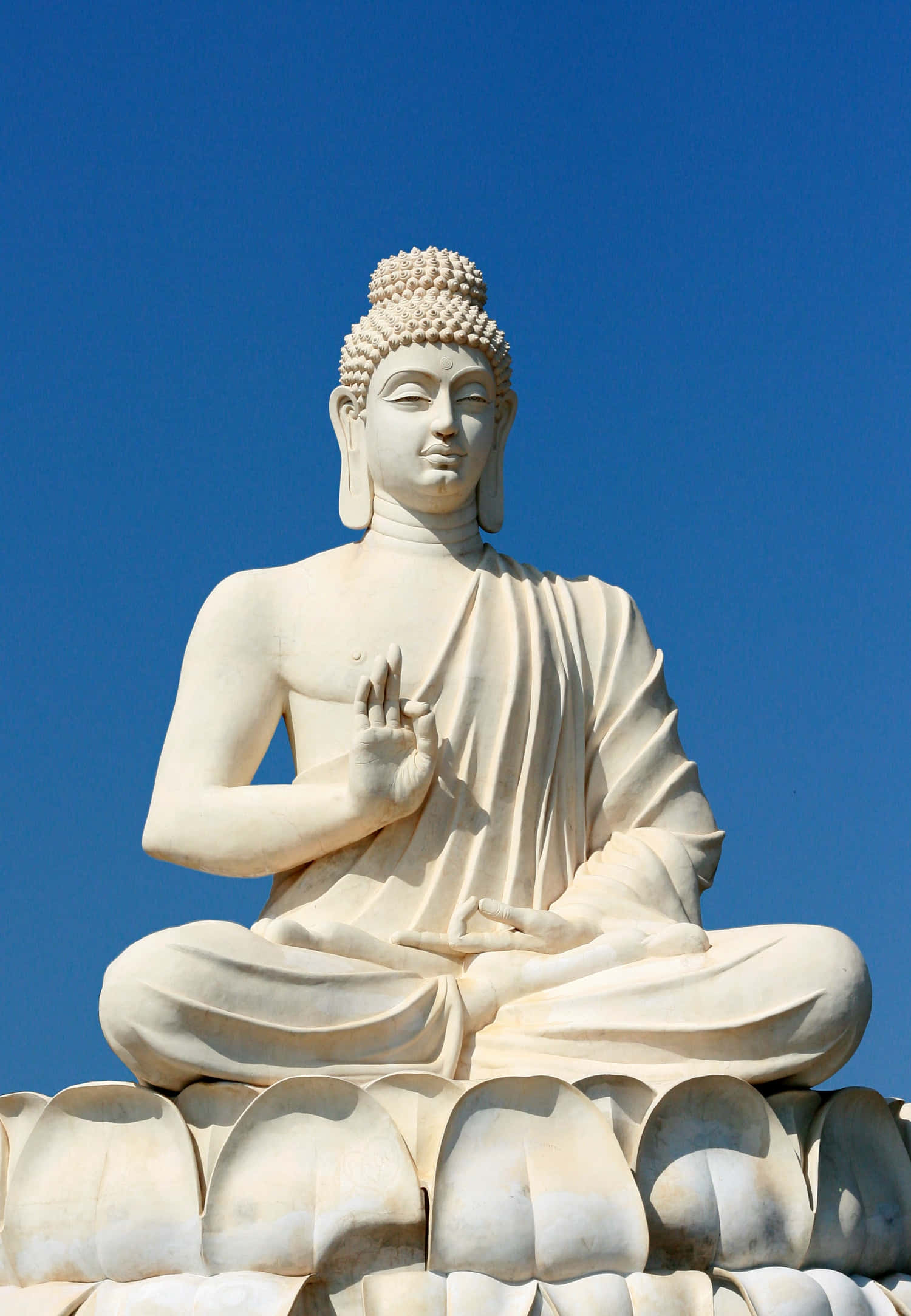 Gautama Buddha 桌布 壁紙 — 一尊寧靜的白色佛像盤腿坐在蓮花座上，背景是清澈的藍天。