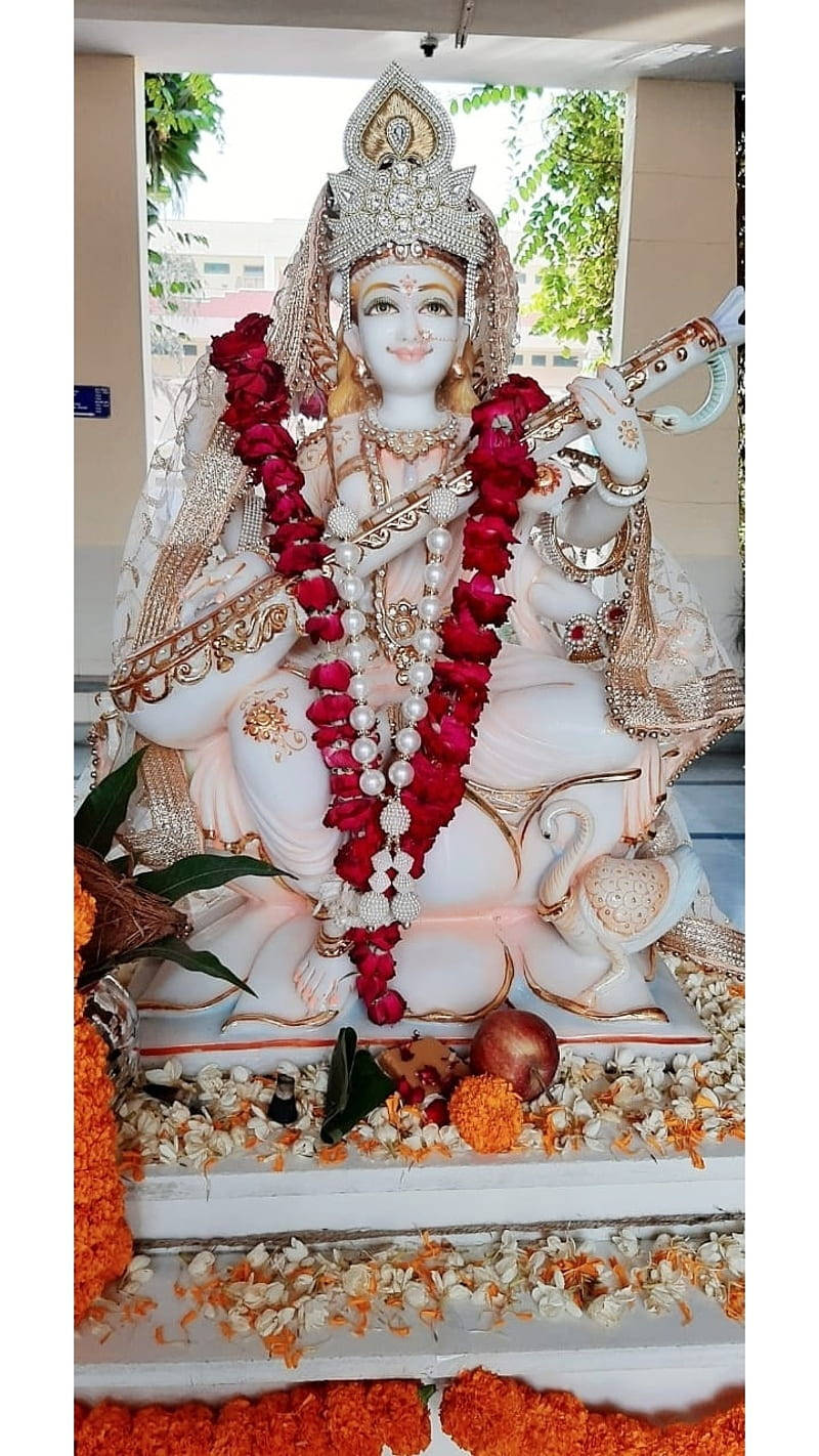 Saraswati Mata 桌布 壁紙 — 一尊寧靜的白色大理石克里希納神像，飾有紅色和白色花環，手持長笛，坐在天鵝旁邊。