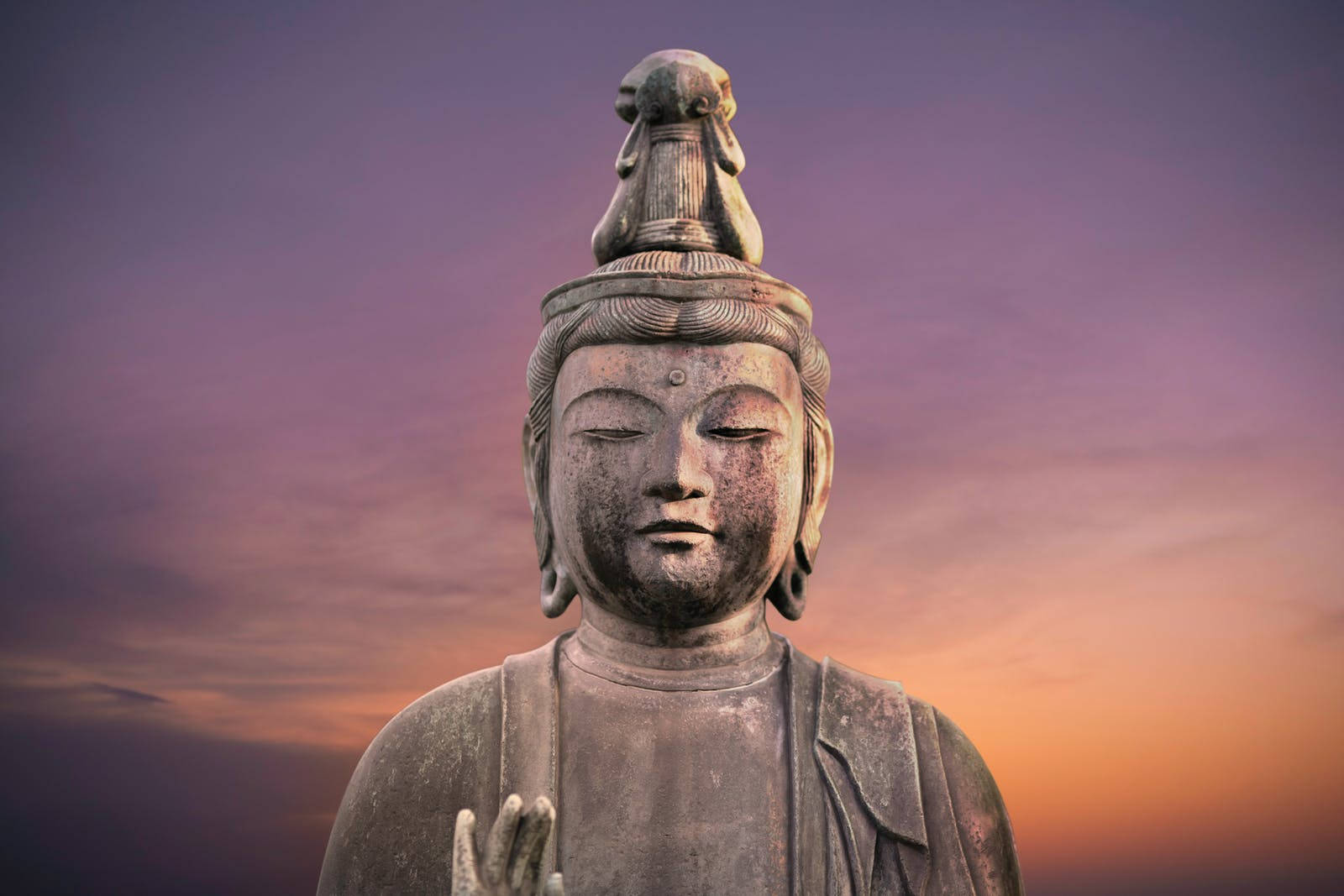 Gautam Buddha 桌布 壁紙 — 一尊寧靜的石佛像，閉著眼睛，頭頂有一頭獅子，背景是紫色和橙色的暮色天空。