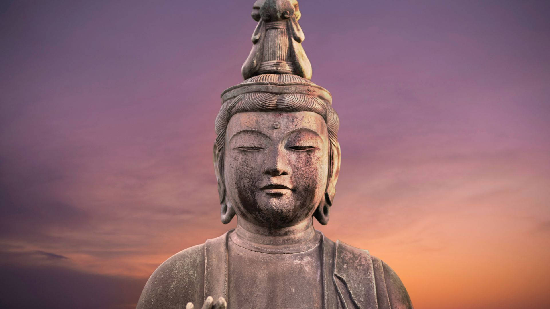 god laptop 桌布 壁紙 — 一尊寧靜的石佛像在柔和紫色和橙色交織的暮色天空中平靜地凝視。