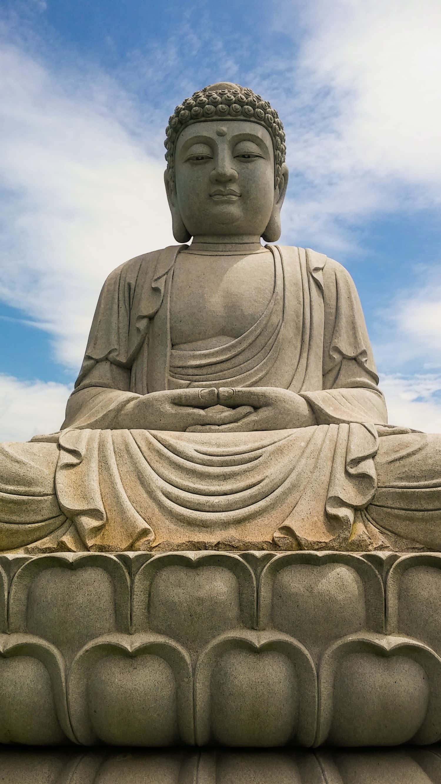 Gautama Buddha 桌布 壁紙 — 一尊寧靜的石佛像在藍天白雲下盤腿坐在蓮花座上。
