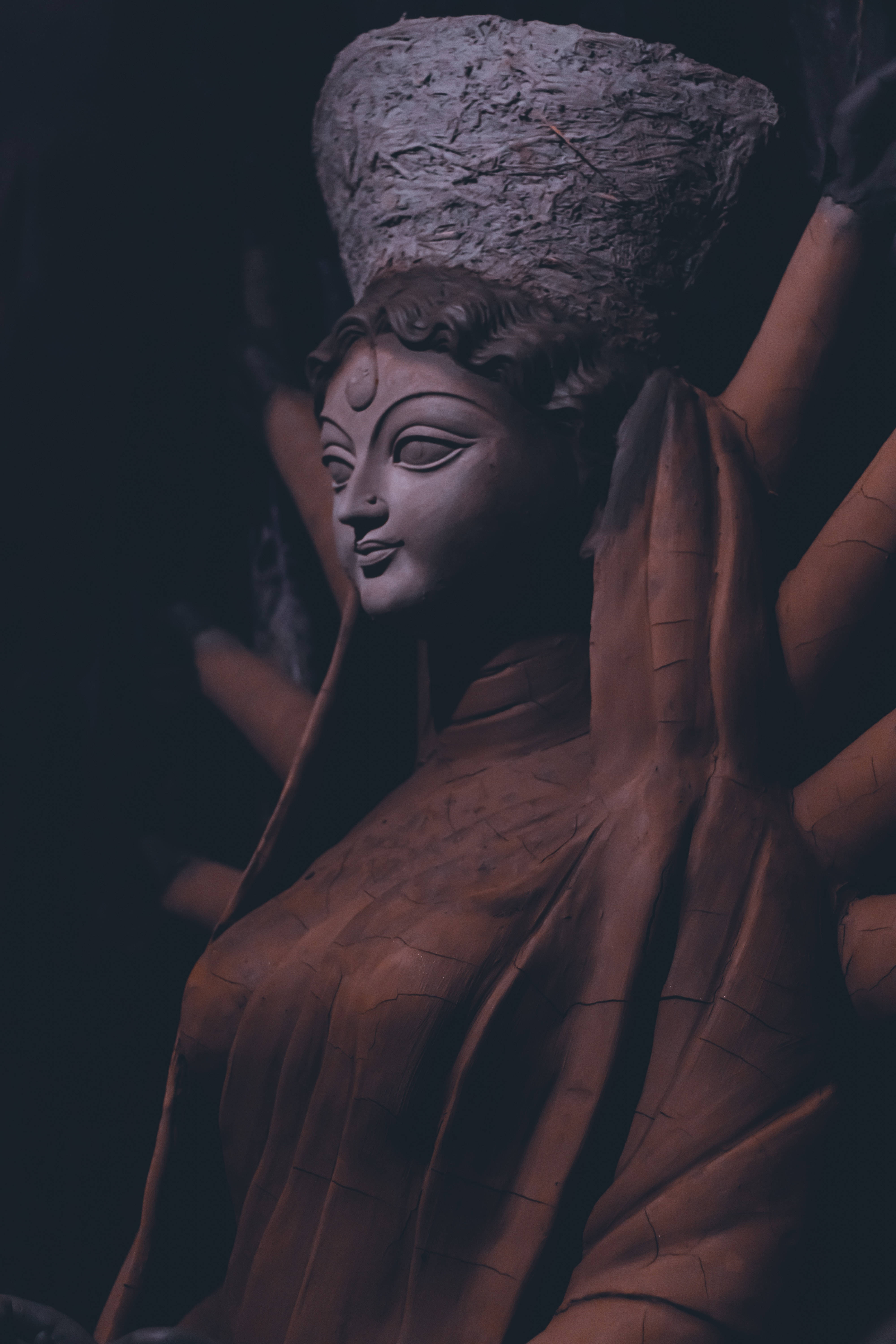 Sculpture 桌布 壁紙 — 一尊寧靜的石像，神祇戴著紋理王冠，身披垂墜長袍，在黑暗背景中由柔和的方向性光線照亮。