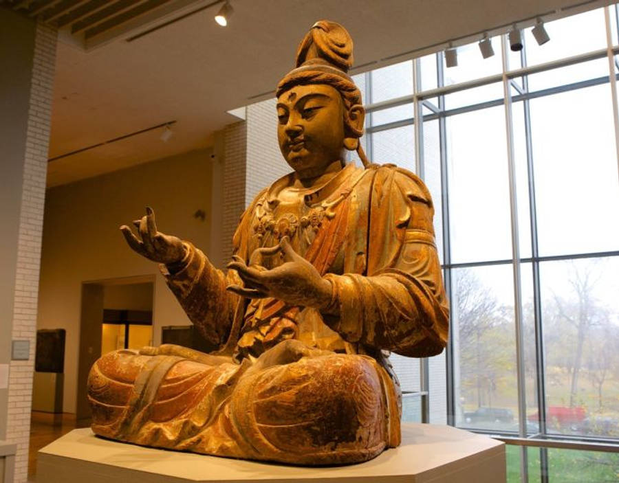 Minneapolis 桌布 壁紙 — 一尊寧靜的金色佛像在博物館畫廊中盤腿而坐，大窗戶顯露出外面的秋樹。