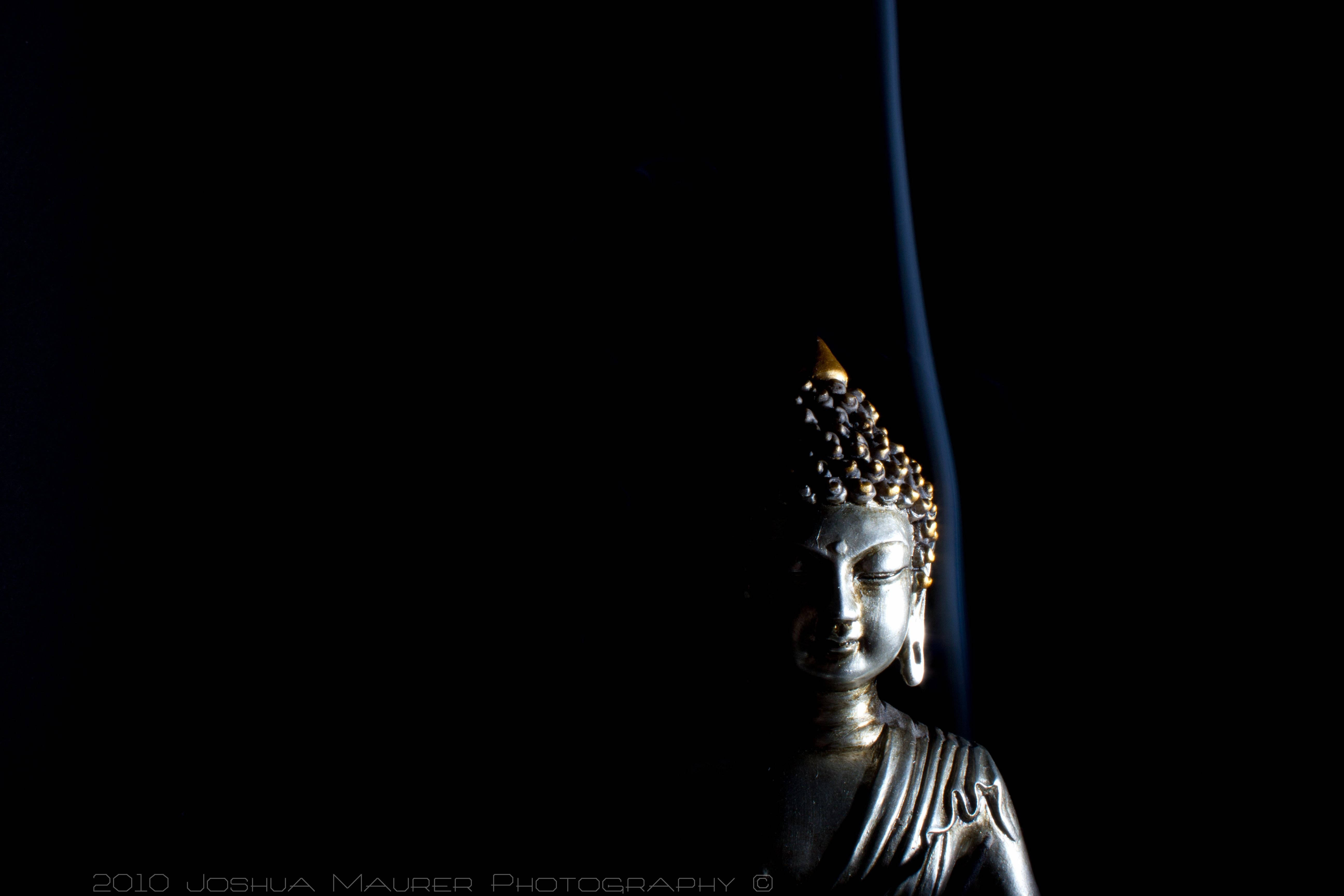 black buddha 桌布 壁紙 — 一尊寧靜的銀色佛像，在深黑色背景上被柔和光線照亮，並帶有一條細藍色煙霧痕跡。