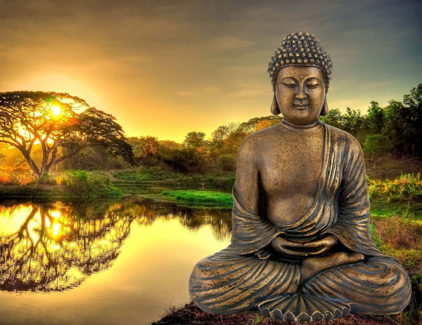 佛陀 桌布 壁紙 — 一尊寧靜的青銅佛像坐在寧靜的池塘邊，金色夕陽下，樹影在水中閃爍。
