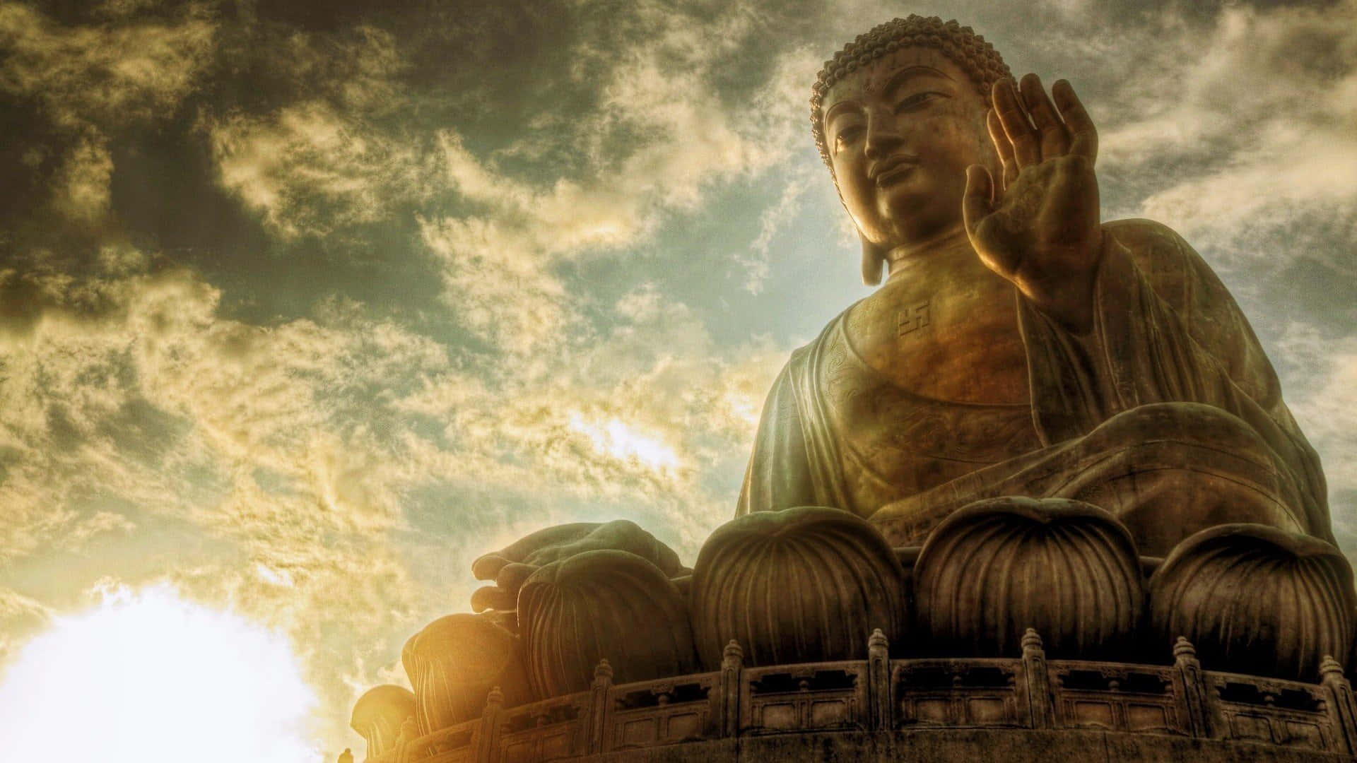 一尊巨大的佛像沐浴在金色的日出光中，背景是多雲的天空。 — 佛陀 GIF 壁紙