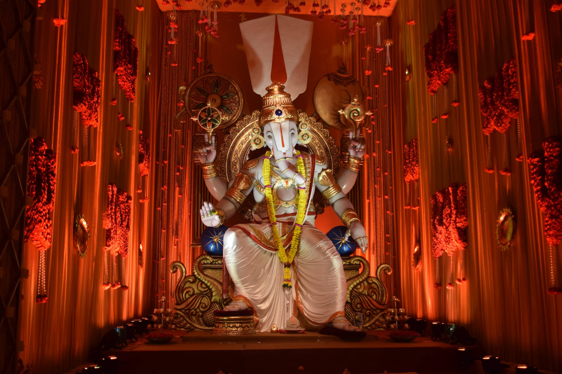 Ganesh 桌布 壁紙 — 一尊巨大的白色象神像，飾有黃金首飾和黃色花環，在溫暖的紅色燈光下莊嚴地坐在華麗的寶座上。