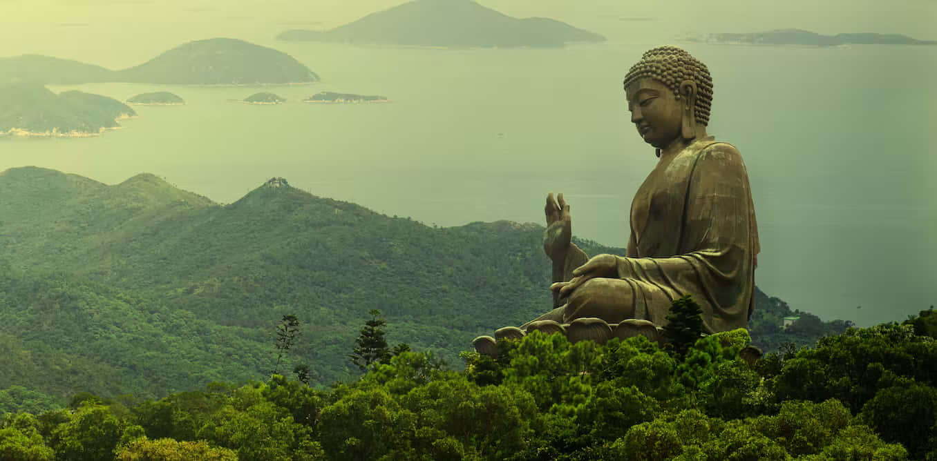 佛陀 桌布 壁紙 — 一尊巨大的金色佛像寧靜地坐在鬱鬱蔥蔥的綠色山頂上，俯瞰著霧氣瀰漫的海洋和遙遠的島嶼。