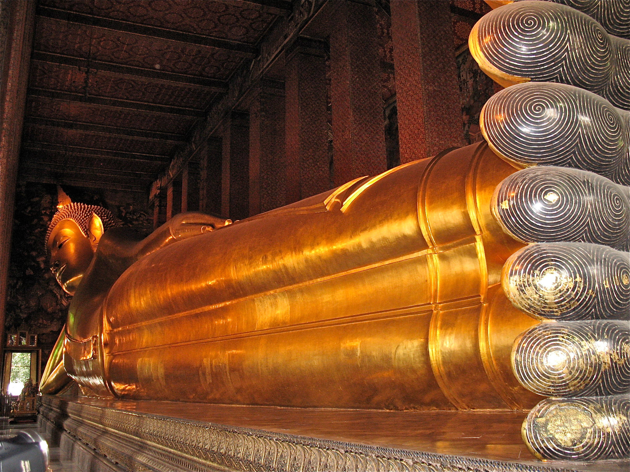 Bangkok 桌布 壁紙 — 一尊巨大的金色臥佛在擁有複雜木結構和溫暖環境照明的寺廟中寧靜地安息。