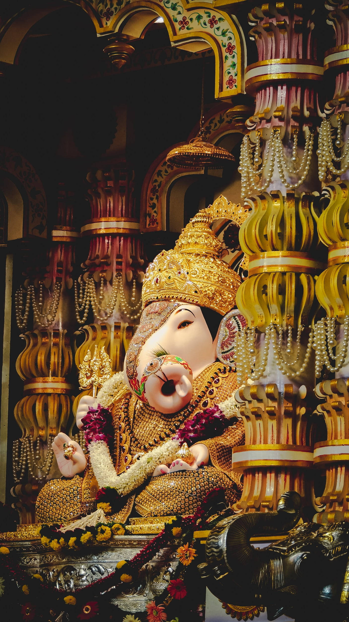 ganesh iPhone 桌布 壁紙 — 一尊巨大的金色象神像，飾以鮮花和珠寶，莊嚴地坐在華麗的寺廟神龕中。