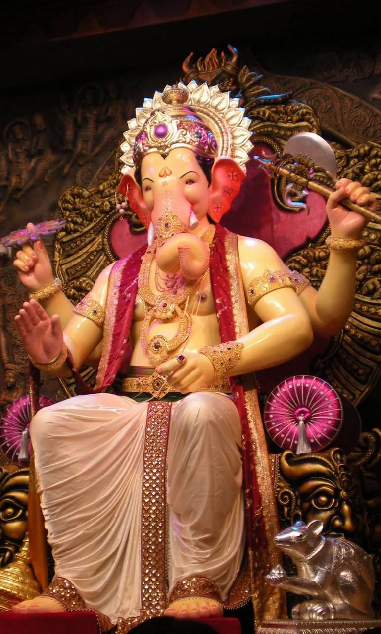 Hindu Temple 桌布 壁紙 — 一尊巨大的金色象神雕像，飾有珠寶和粉紅色布料，威嚴地坐在華麗的寶座上，腳邊有一隻銀色老鼠。