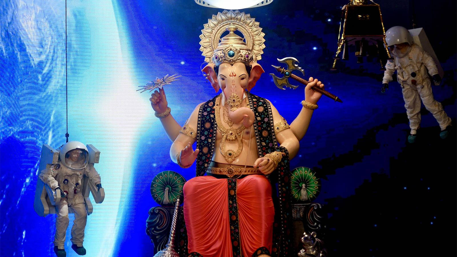 Hindu Temple 桌布 壁紙 — 一尊巨大的金色象神雕像在太空中威嚴地坐著，兩旁有太空人和月球登陸器，背景是一顆發光的藍色行星。