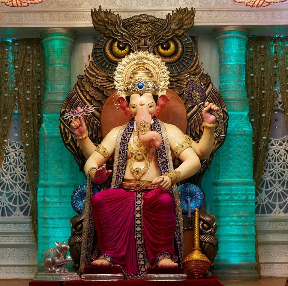 Hindu Temple 桌布 壁紙 — 一尊巨大的金色象頭神像，有象頭和四臂，坐在由貓頭鷹翅膀和藍綠色柱子環繞的寶座上。