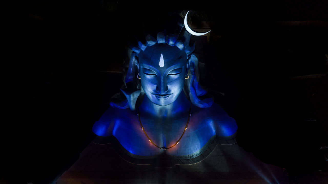 shiva iPhone 桌布 壁紙 — 一尊帶有新月冠冕的寧靜藍色發光神像，在漆黑的背景下閃耀。