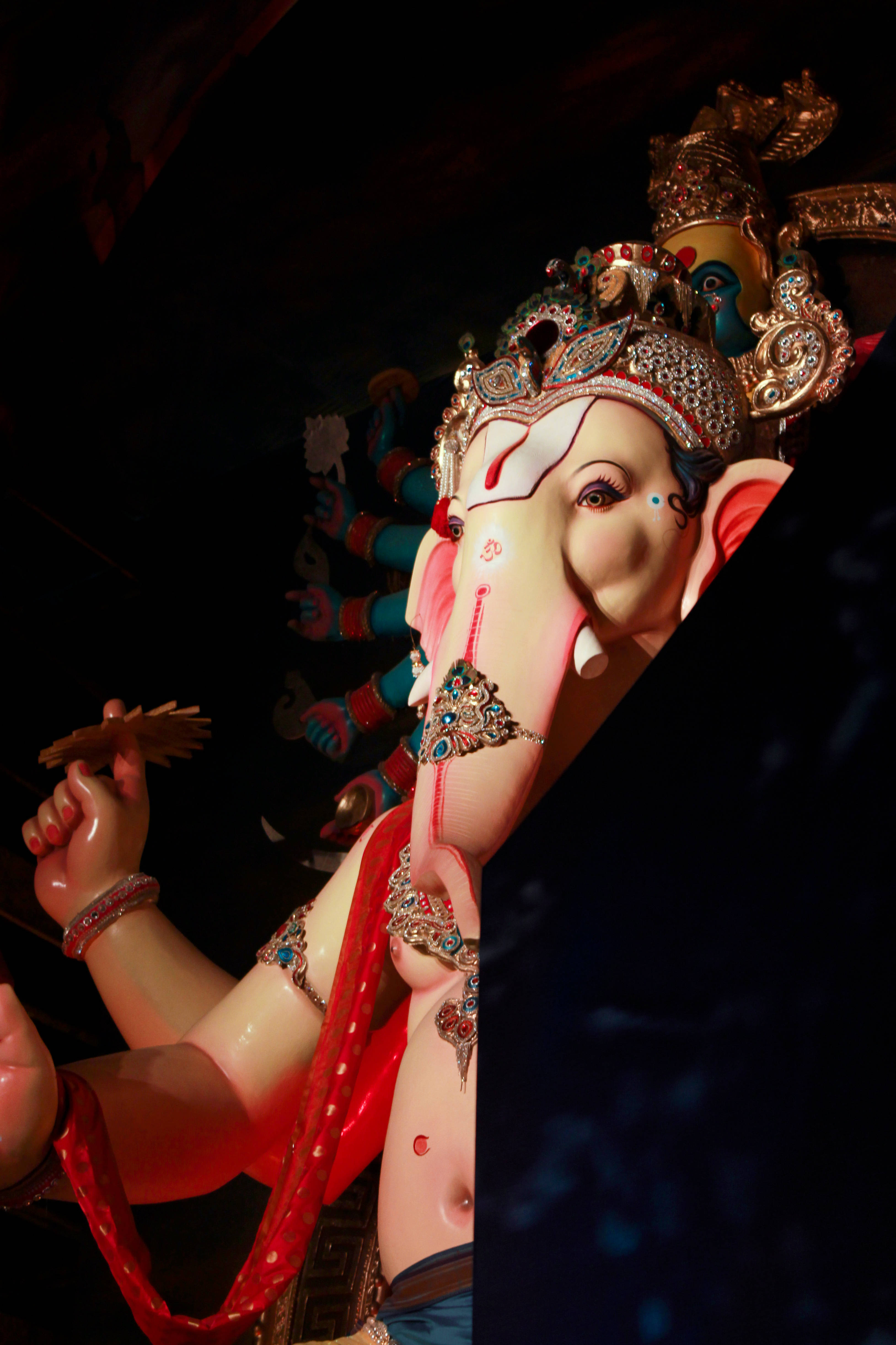 Bappa 桌布 壁紙 — 一尊明亮照明的華麗象頭神像，帶有粉紅色調和精緻的金飾，背景為深色。