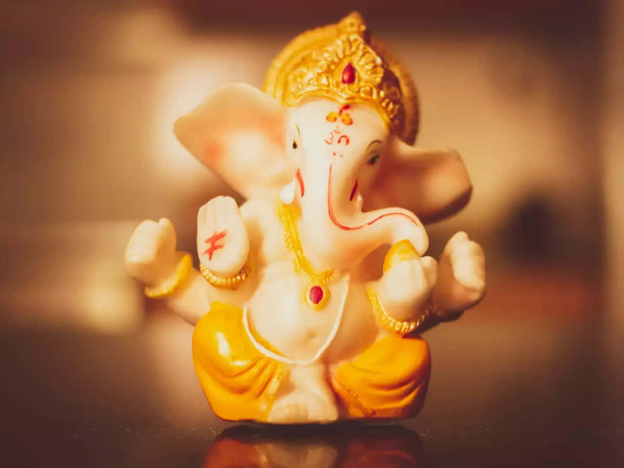 Ganesh Chaturthi 桌布 壁紙 — 一尊溫暖照明的白色象頭神像，飾有黃金珠寶和紅色標記，寧靜地坐在反光表面上。
