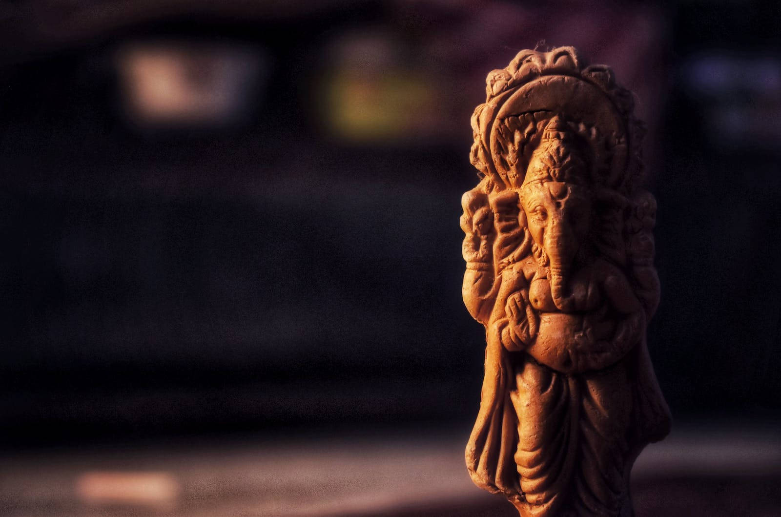 Ganesh 桌布 壁紙 — 一尊溫暖照明的象神黏土雕像，在黑暗模糊的背景中以淺景深呈現。