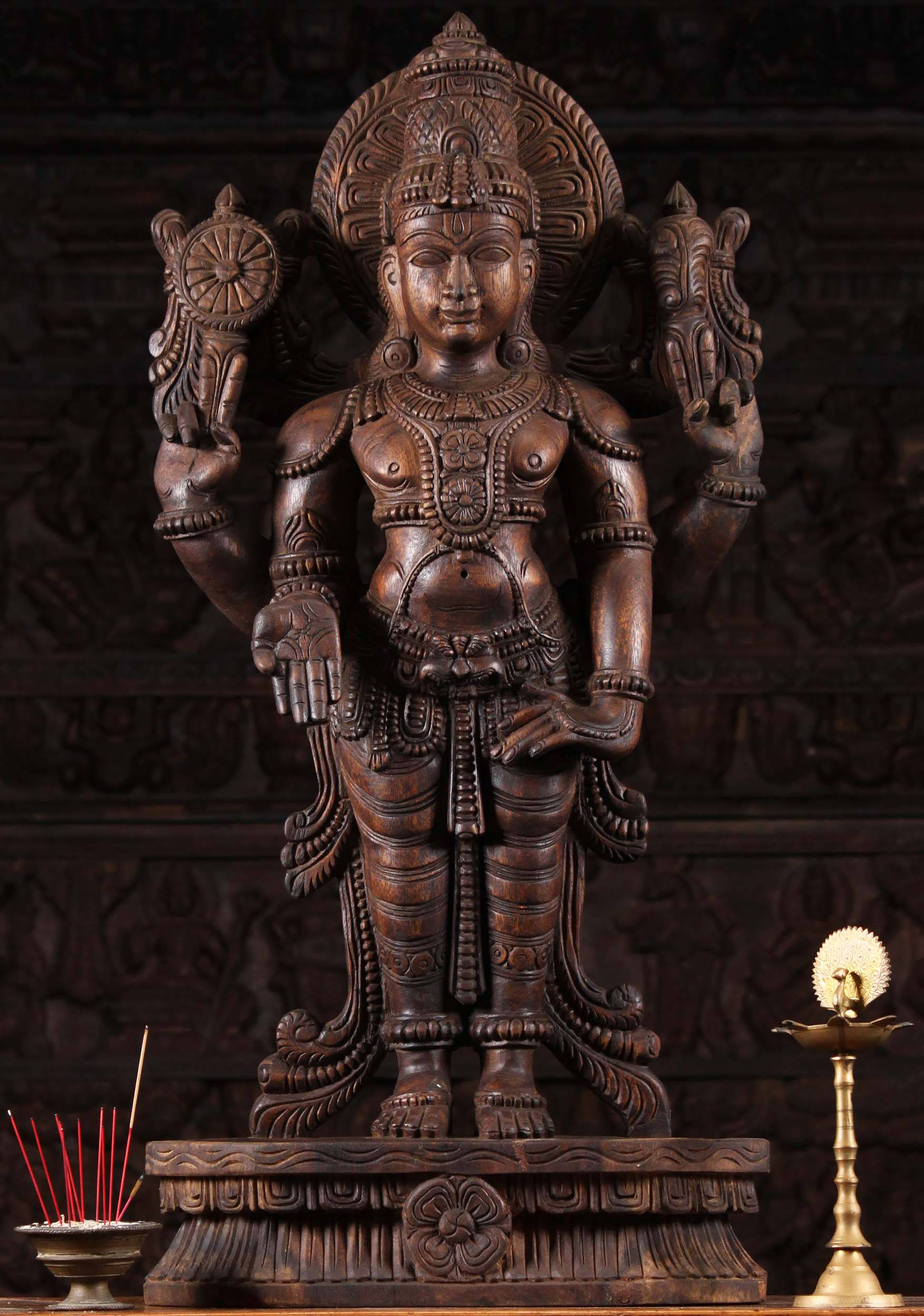 Sculpture 桌布 壁紙 — 一尊精細的木雕多臂神像，飾有華麗的頭飾和珠寶，立於雕刻精緻的基座上，旁邊有香和黃銅油燈。