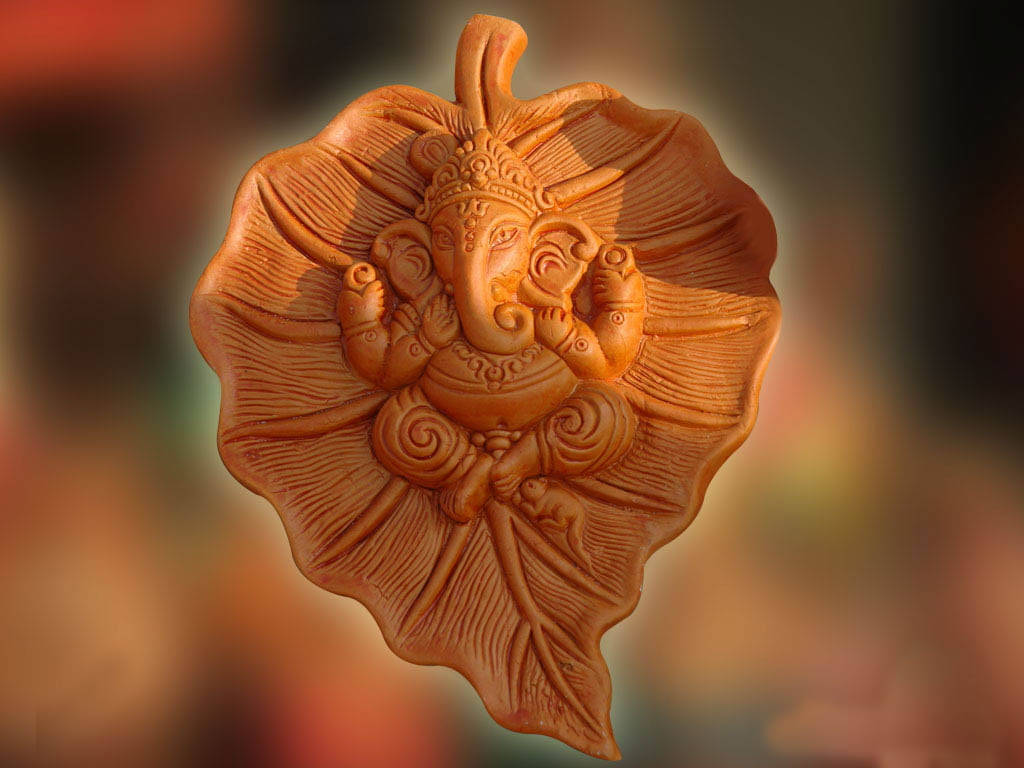 葉子 桌布 壁紙 — 一尊精細的象神迦尼薩赤陶雕塑，精雕細刻在葉形底座上，帶有溫暖的金色燈光。